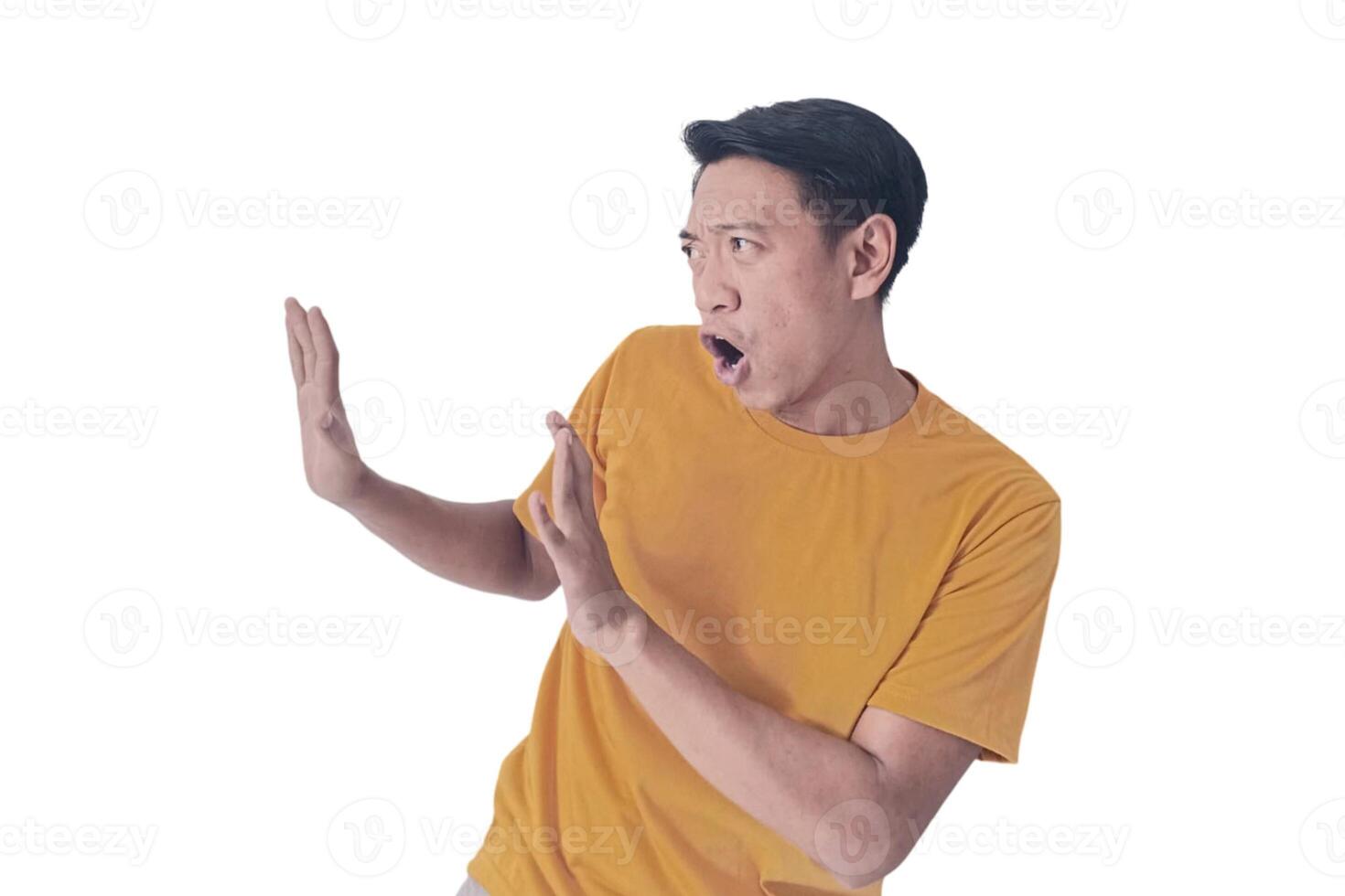 Portrait of an Asian man wearing a orange T-shirt, expressing surprise and shock with open palms, isolated against a white background. photo