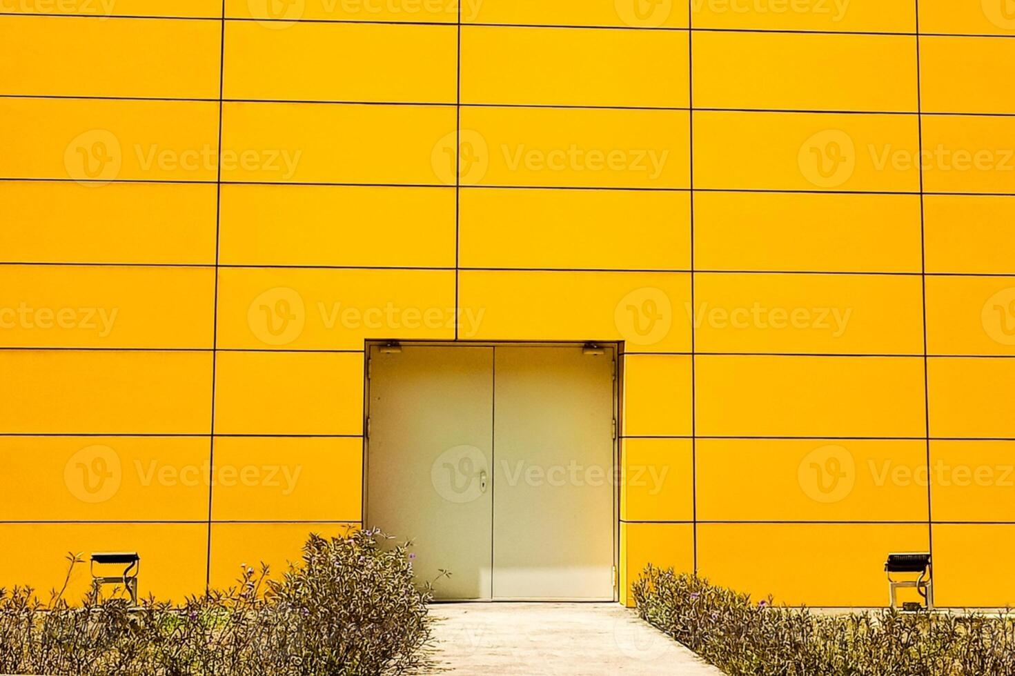 portrait of a yellow wall with an emergency door in the middle.The bright facade of the building is sheathed in aluminum with one glass door photo