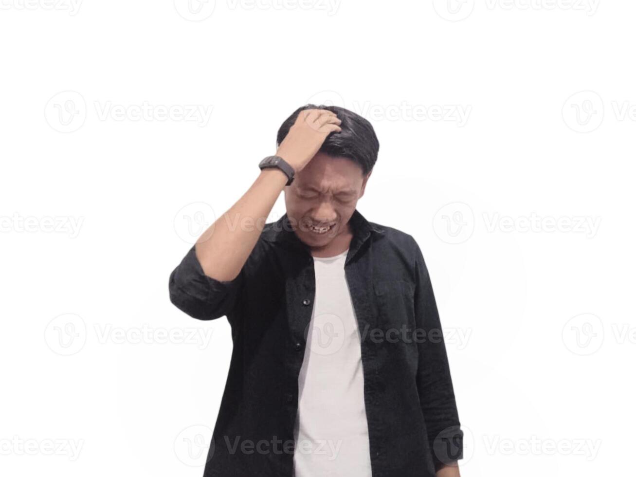 A man in a black shirt holds his head with a pained expression, indicating a headache or discomfort. The plain white background emphasizes his distress and highlights his posture and expression. photo