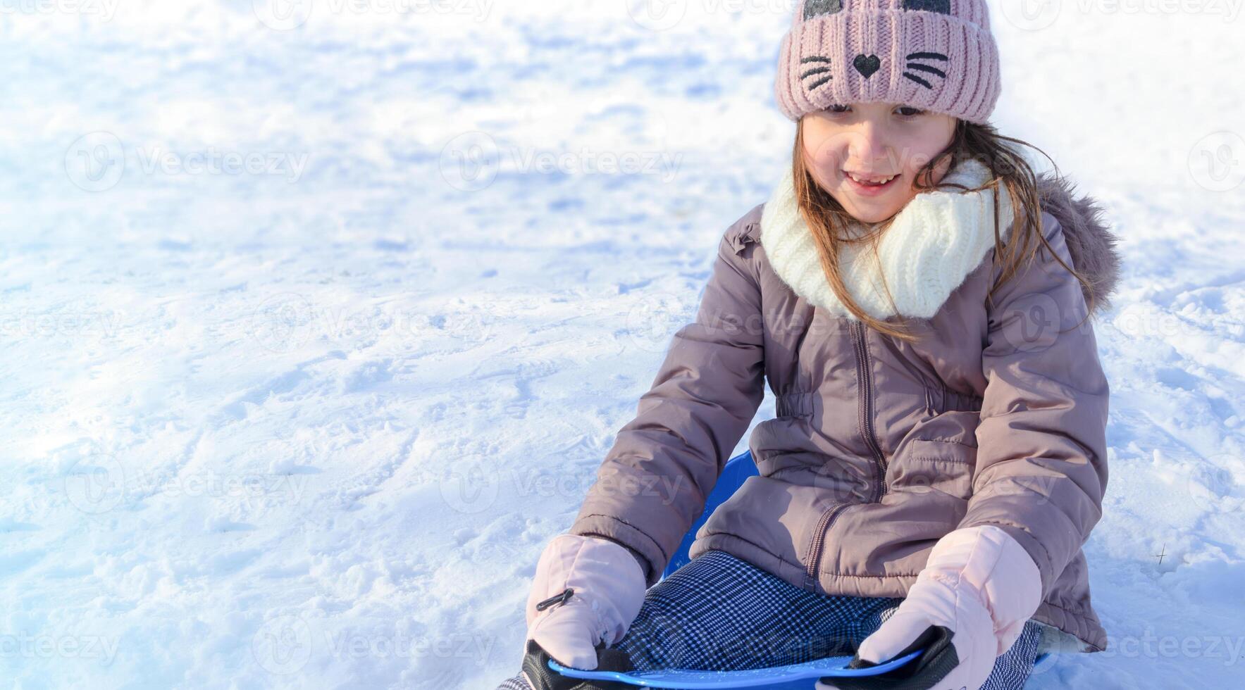 Young girl enjoying a day of sledding on a snowy hill in wintertime sunshine photo