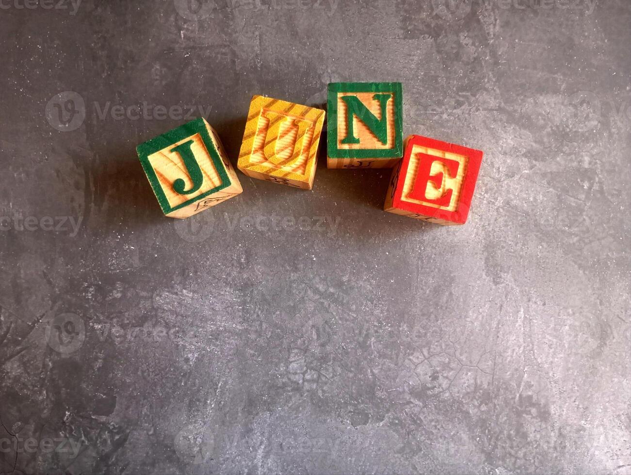 A photo of a wooden block with the words june written on it, styled in isolation with space for text.