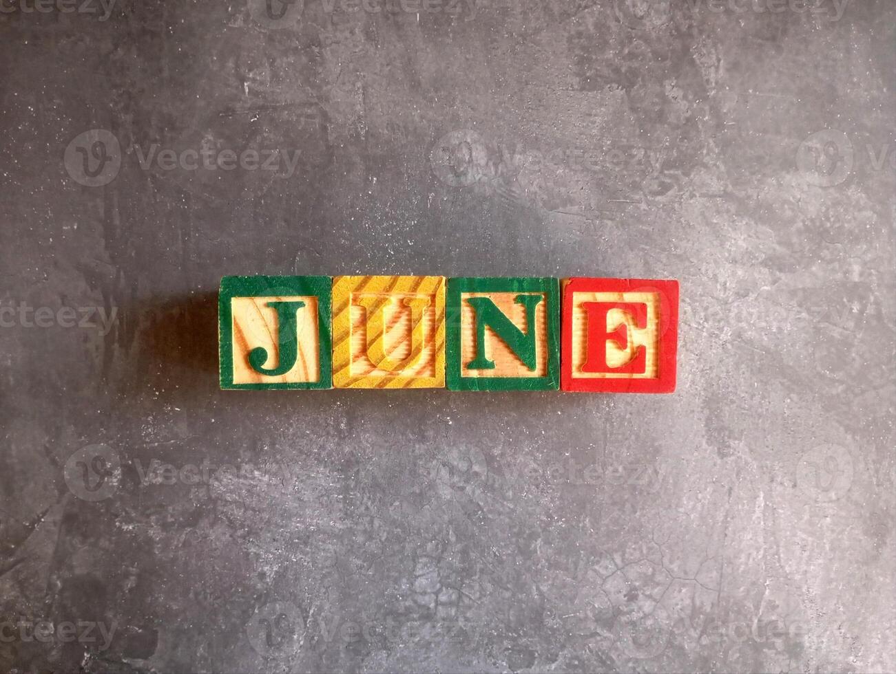 A photo of a wooden block with the words june written on it, styled in isolation with space for text.