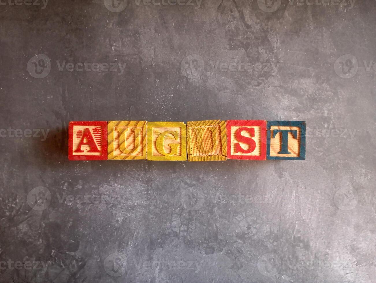 A photo of a wooden block with the words august written on it, styled in isolation with space for text.