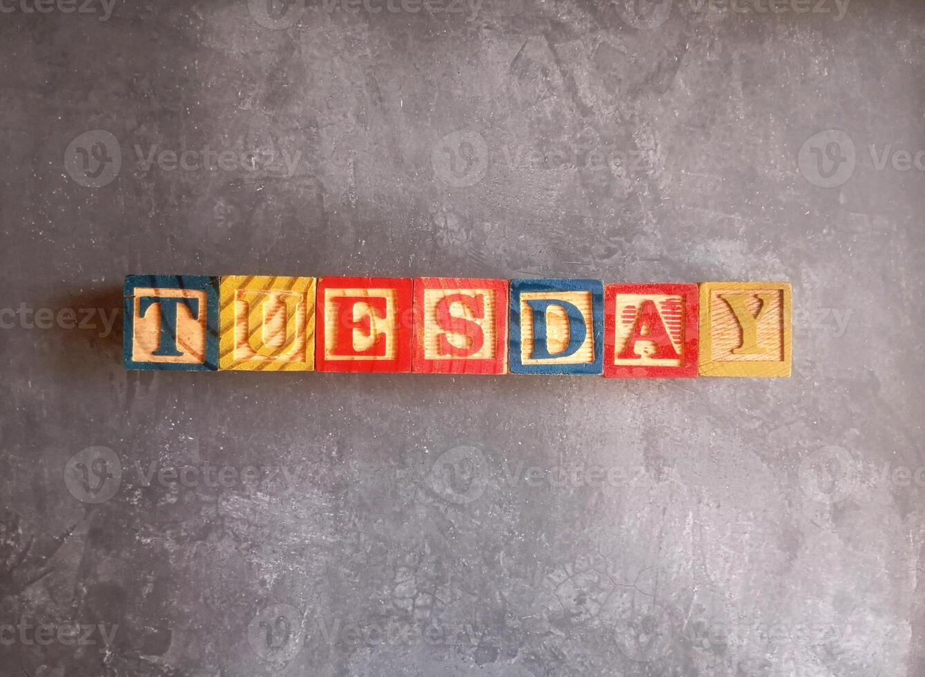 A photo of a wooden block with the words tuesday written on it, styled in isolation with space for text.