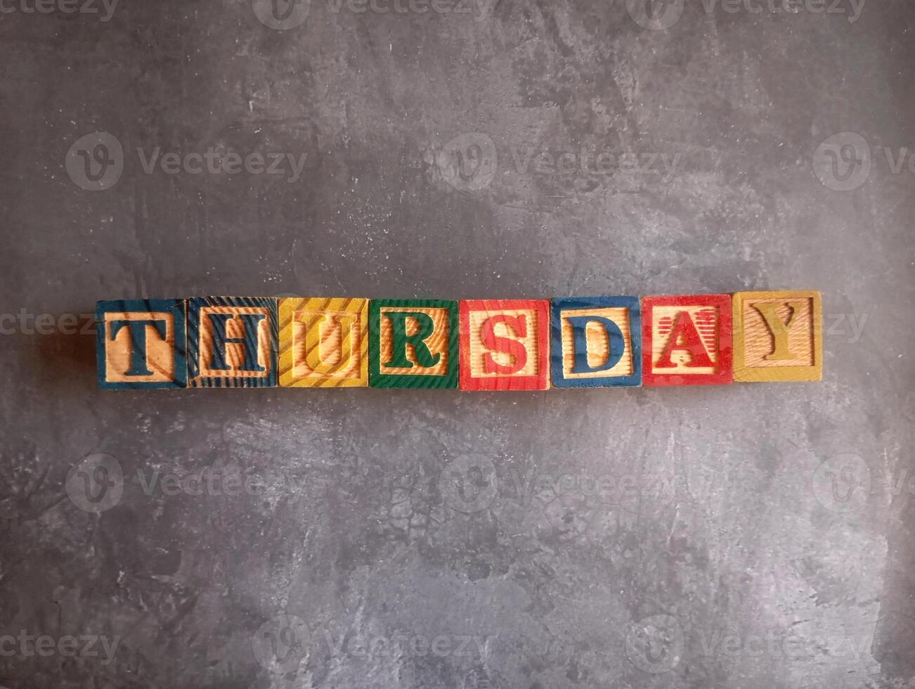 A photo of a wooden block with the words thursday written on it, styled in isolation with space for text.