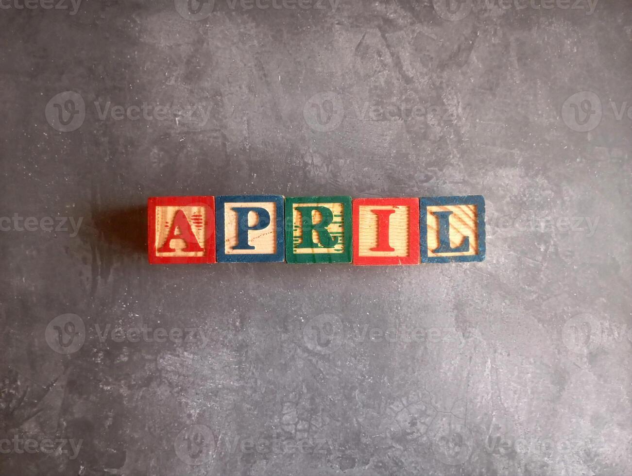 A photo of a wooden block with the words April written on it, styled in isolation with space for text.