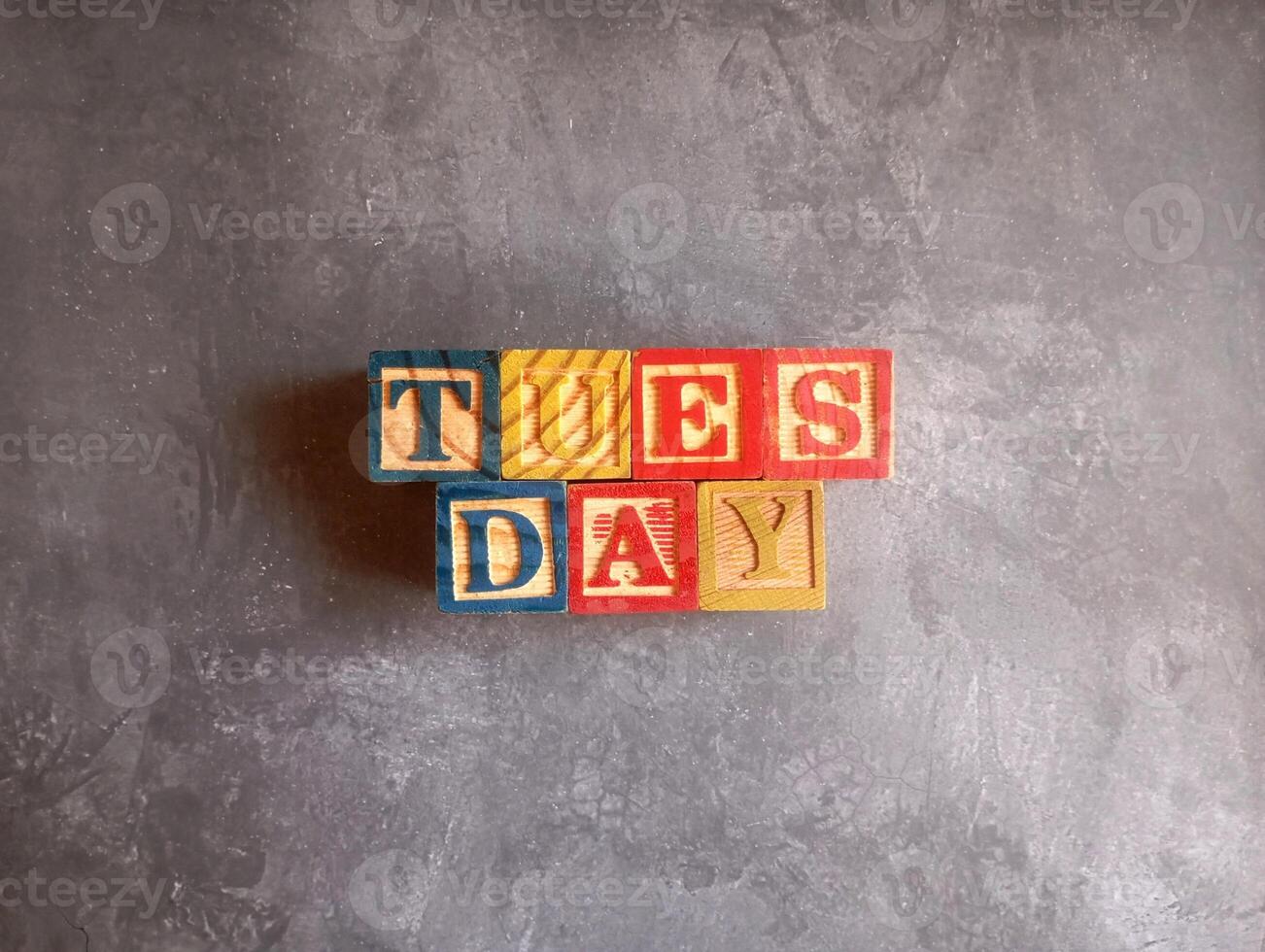 A photo of a wooden block with the words tuesday written on it, styled in isolation with space for text.