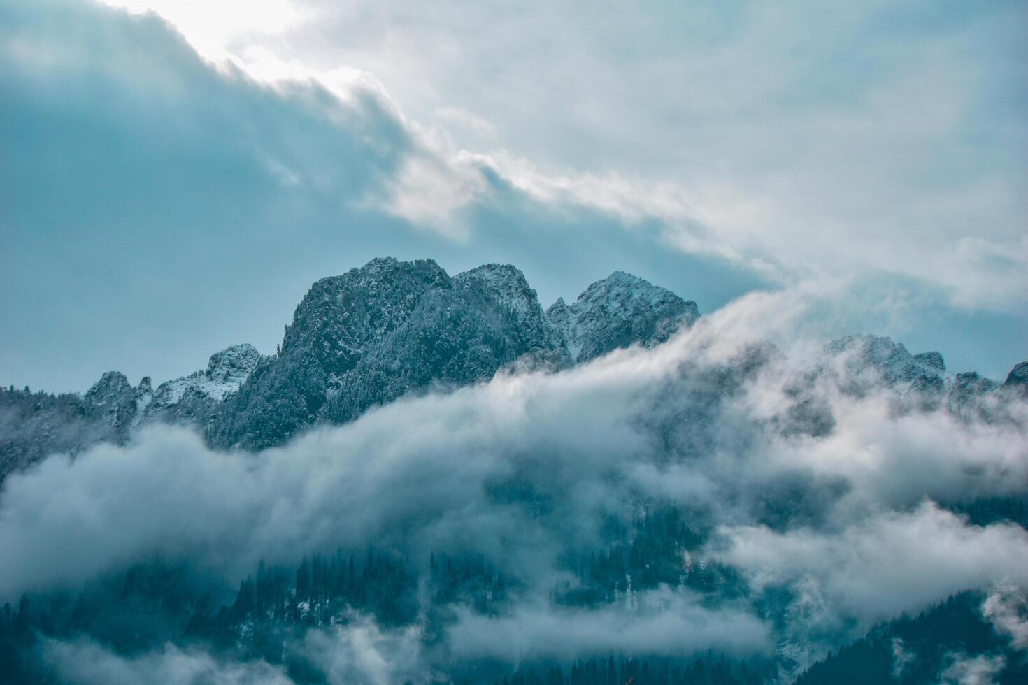 Majestic peaks pierce the azure sky, cloaked in a veil of ethereal clouds. This breathtaking mountain vista beckons us to pause and revel in nature's raw, untamed splendor. photo
