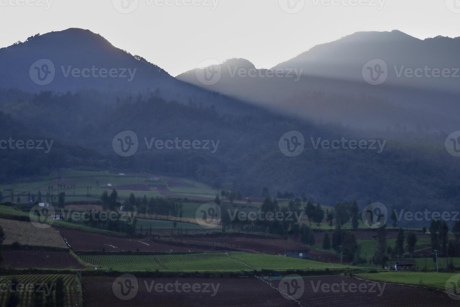 Rays of light come out from the mountain and shine the agricultural valley. Tranquil scene of a countryside in East Java, Indonesia. photo