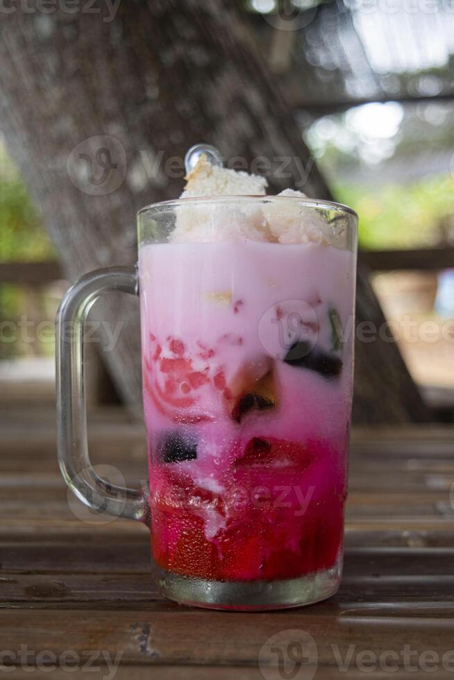 A glass of Es Campur, an Indonesian cold and sweet dessert concoction of fruit cocktails, coconut, tapioca pearls, grass jellies, etc. served in shaved ice, syrup and coconut or condensed milk photo