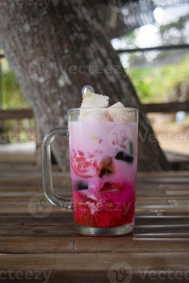 A glass of Es Campur, an Indonesian cold and sweet dessert concoction of fruit cocktails, coconut, tapioca pearls, grass jellies, etc. served in shaved ice, syrup and coconut or condensed milk photo
