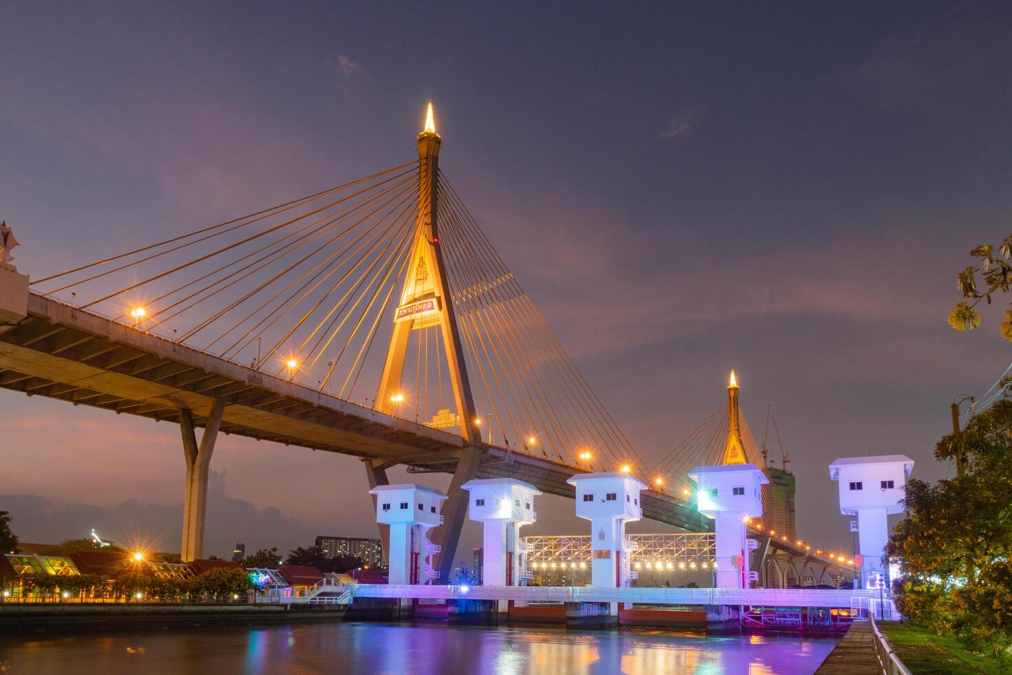 stunning Bhumibol Bridge, illuminated at dusk, showcases its architectural beauty and engineering marvel. vibrant lights reflect on water, creating serene atmosphere photo