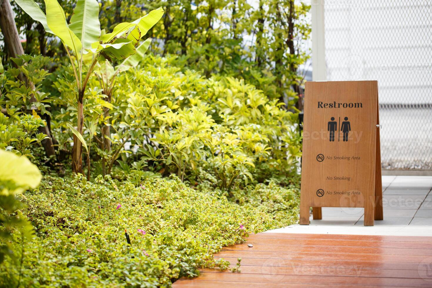 Restroom sign in lush garden setting, surrounded by vibrant greenery and plants, creating serene atmosphere. sign indicates no smoking areas, enhancing peaceful environment photo