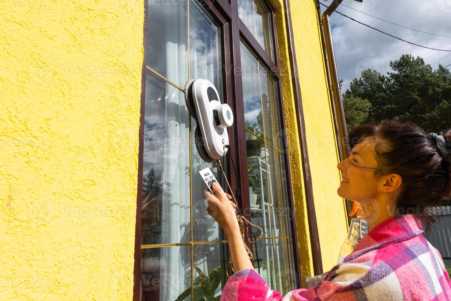 A woman launches a window cleaner robot of the house outside with a yellow facade. Household robotics, household assistant, cleaning servise photo