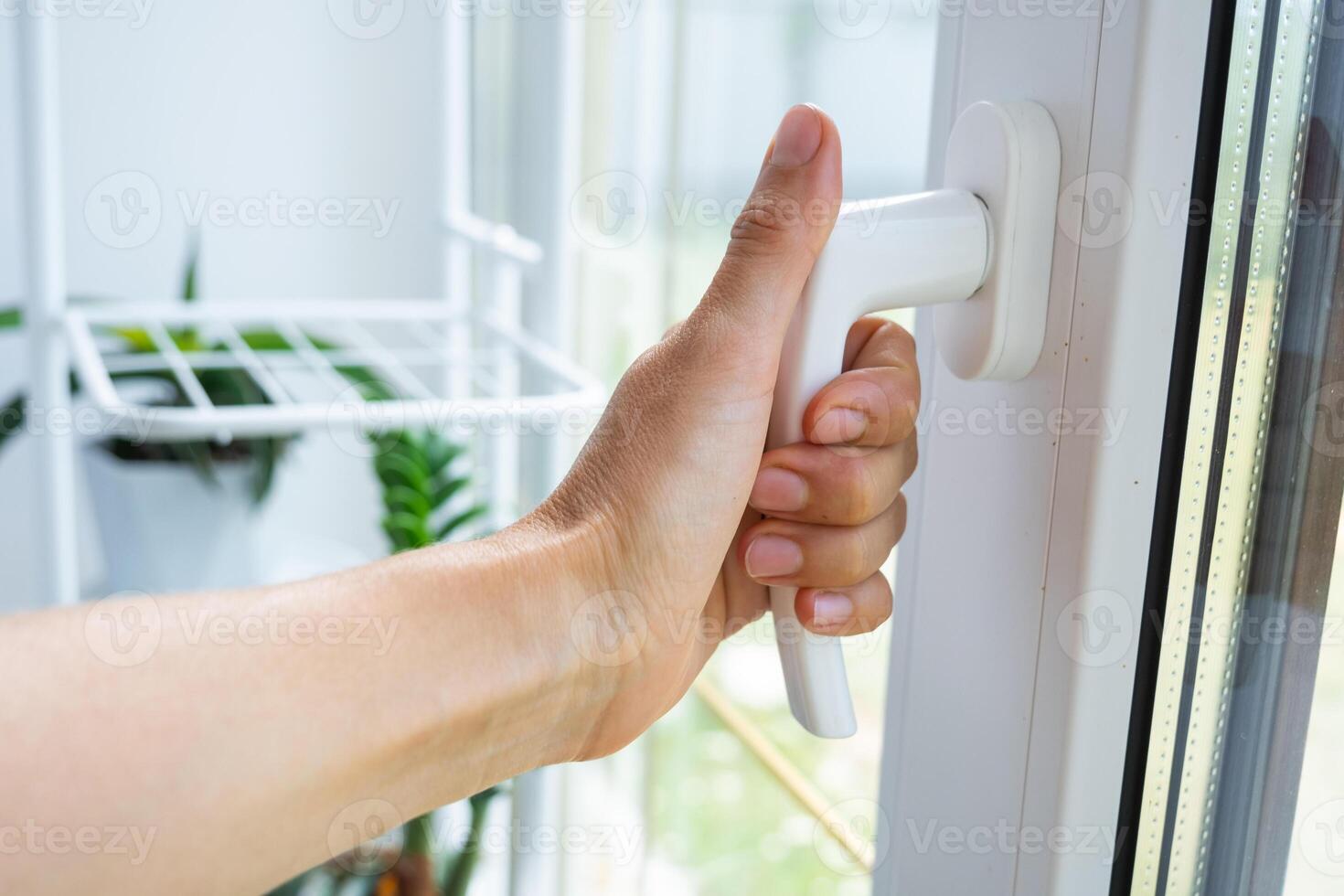 The hand holds the handle of a plastic double-glazed window, closing and opening the window with a rotary mechanism, the position of the handle for ventilation, micro-ventilation photo