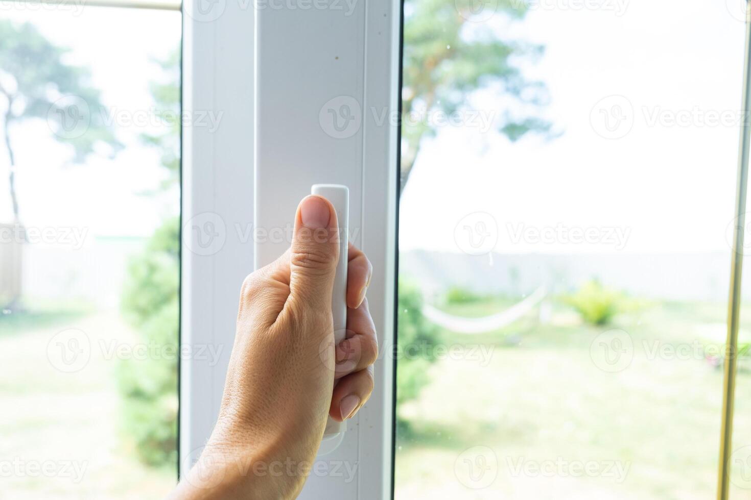 The hand holds the handle of a plastic double-glazed window, closing and opening the window with a rotary mechanism, the position of the handle for ventilation, micro-ventilation photo