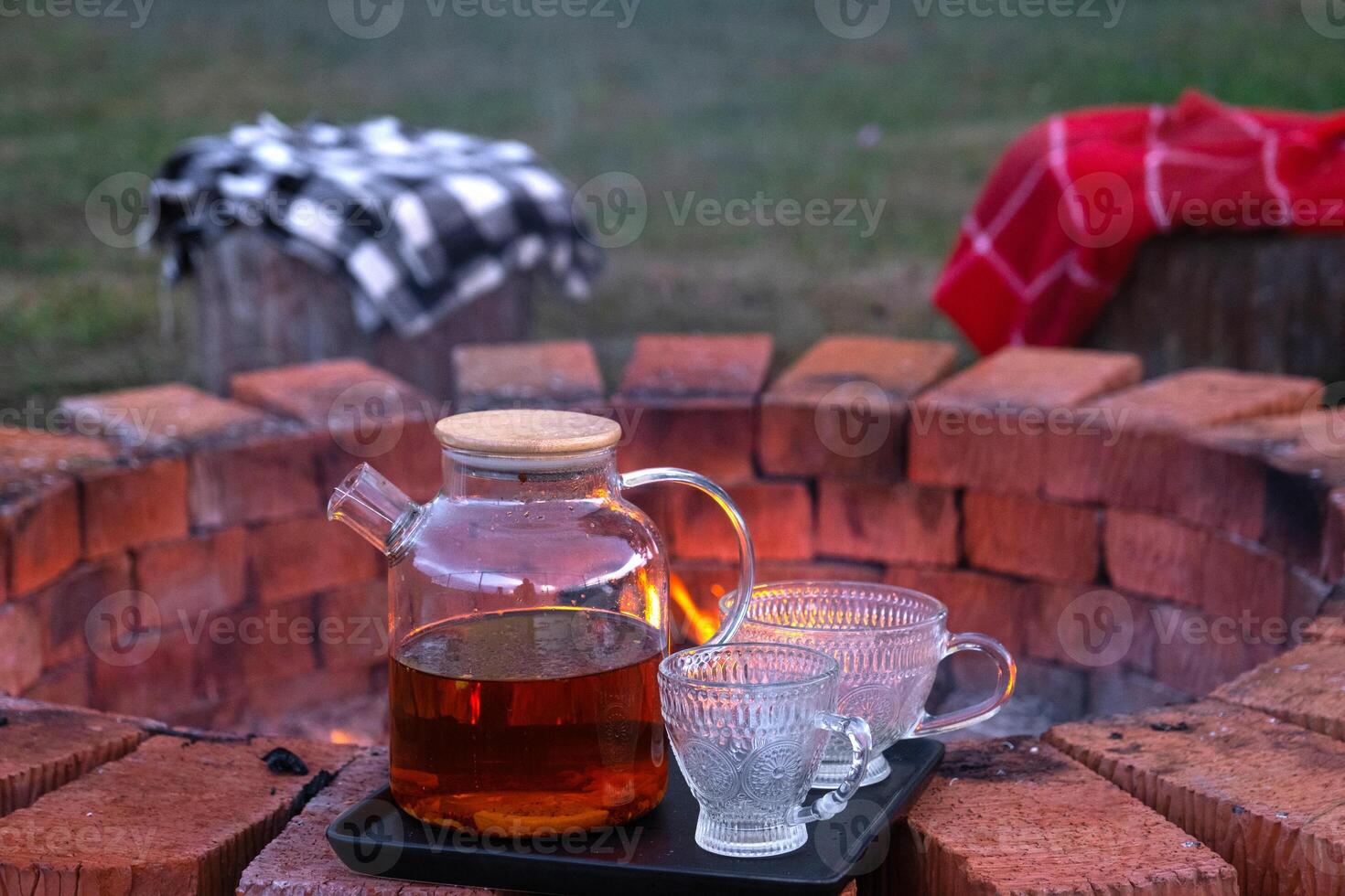 Transparent teapot with tea, cups on a tray on a brick fire pit in the courtyard of the house in a cozy summer evening. photo