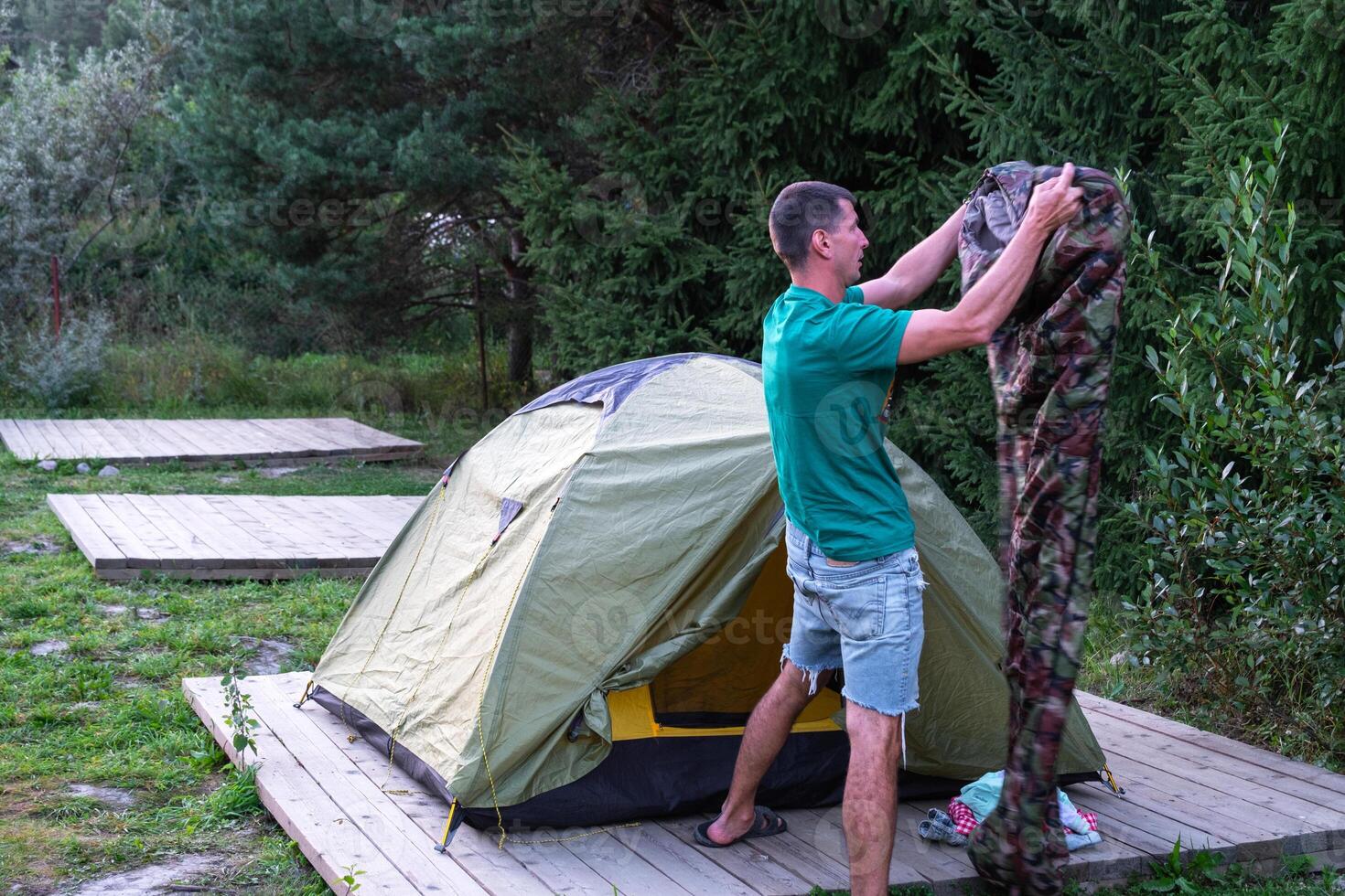 The man installs and assembles tourist tent in a camping in nature in the forest. Domestic tourism, active summer holidays, family adventures. Ecotourism, sport, hike photo