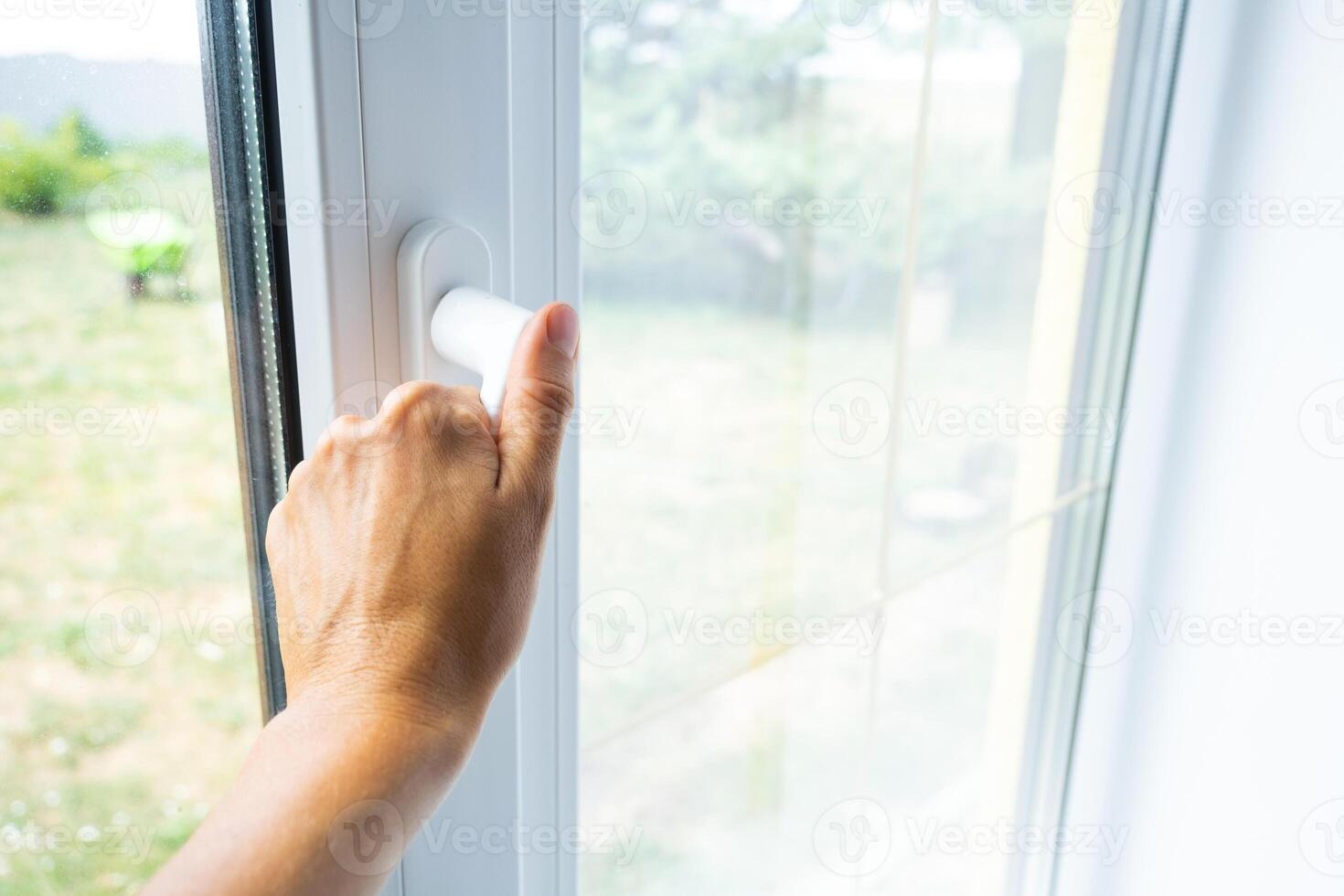 The hand holds the handle of a plastic double-glazed window, closing and opening the window with a rotary mechanism, the position of the handle for ventilation, micro-ventilation photo