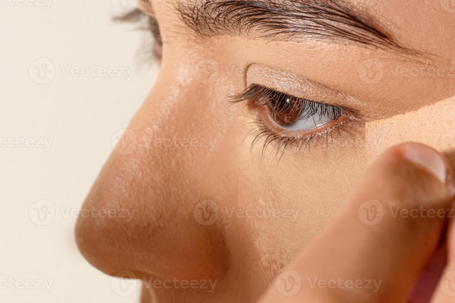 A person's hands using a sponge to spread foundation on a woman's skin. photo