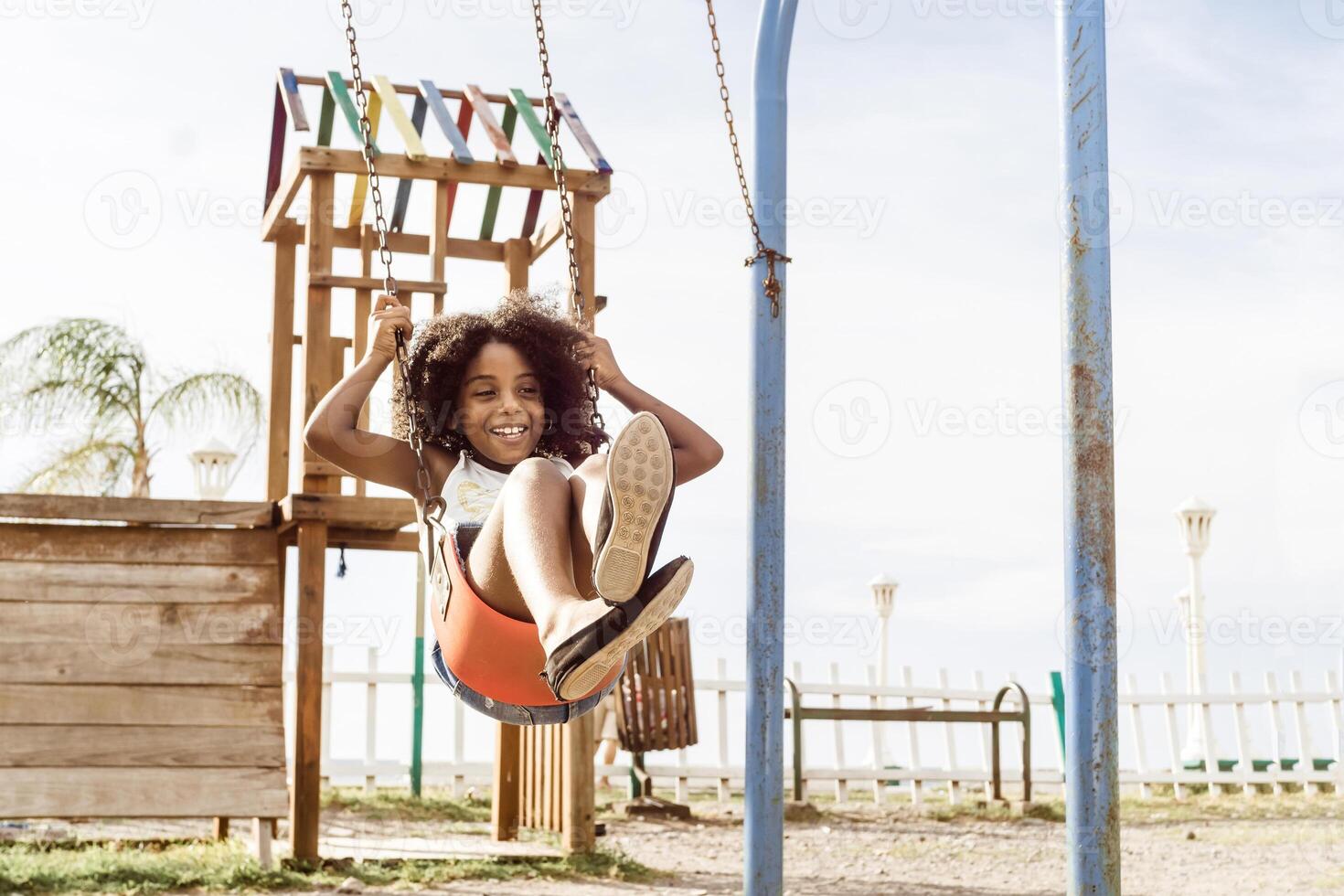 happy and smiling african american girl playing on swing. fun and recreation concept. photo