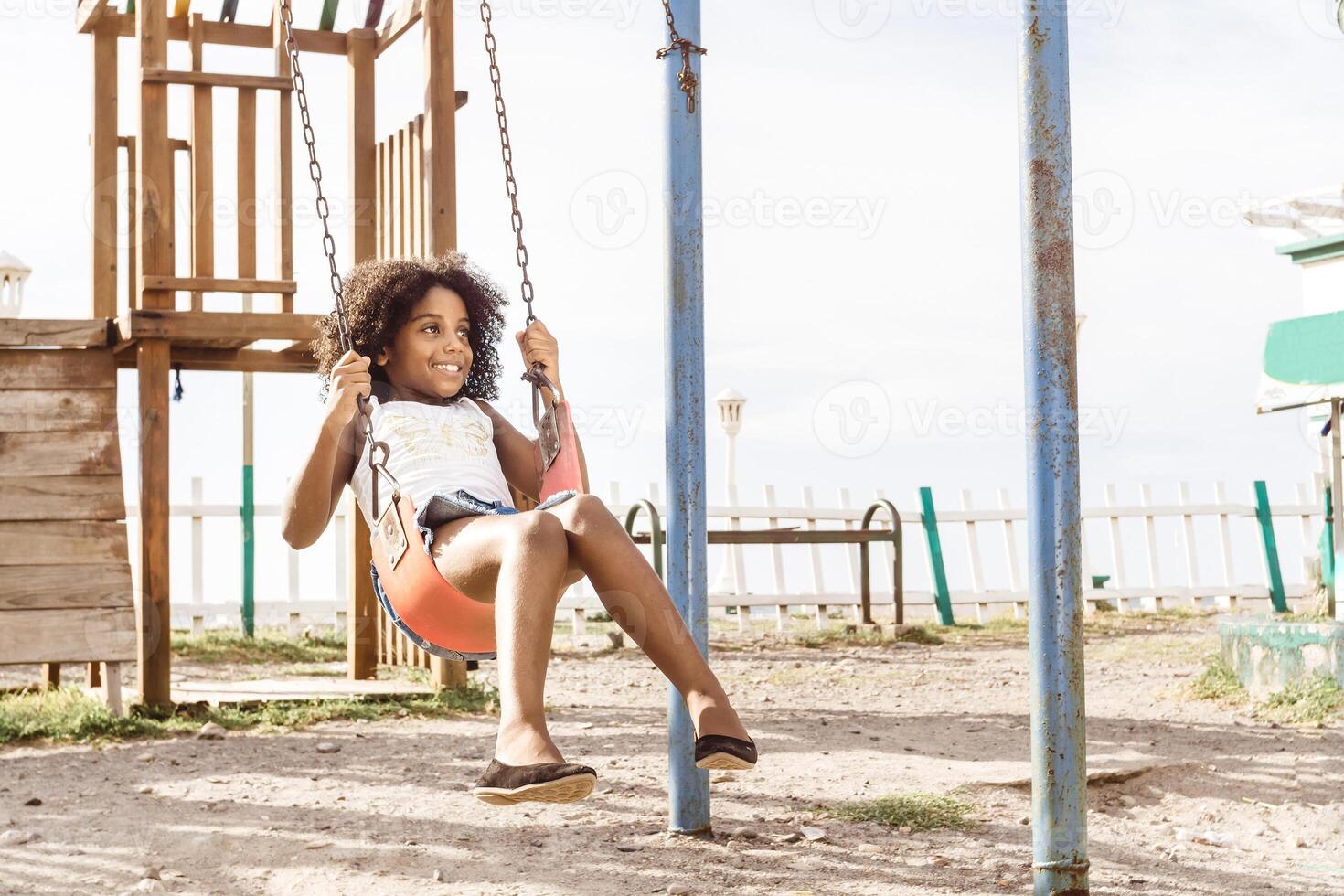 happy and smiling afro american girl playing on swing. fun and recreation concept. photo