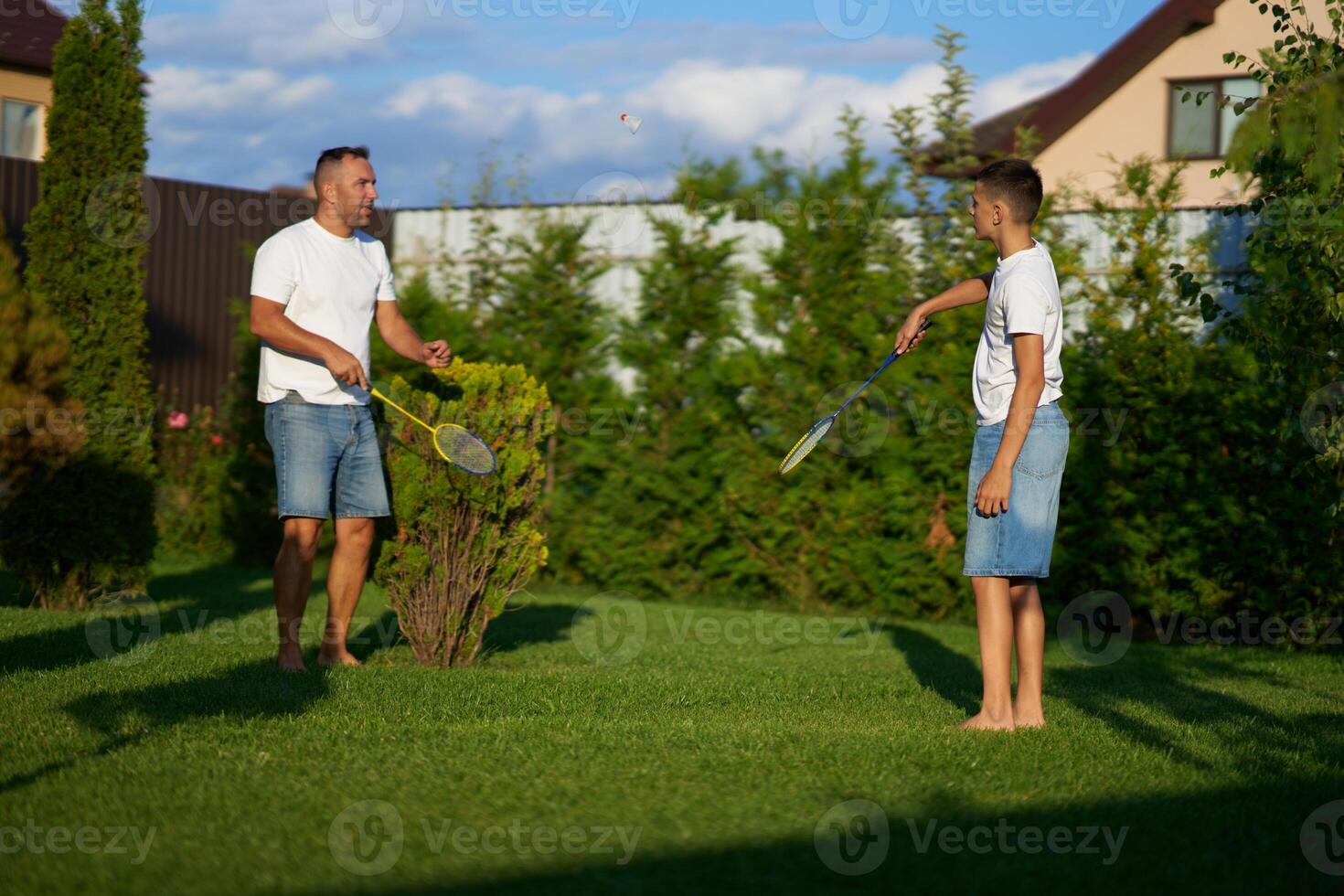 Father and son playing badminton together in a sunny backyard in summer photo