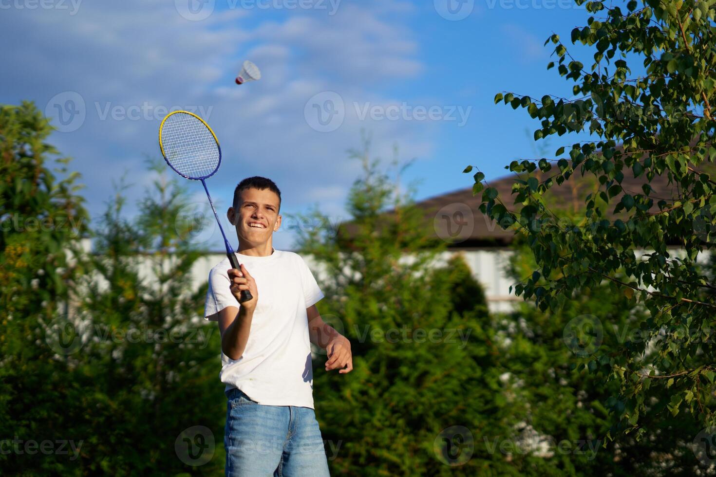 Boy playing badminton outdoors in a sunny backyard with trees photo