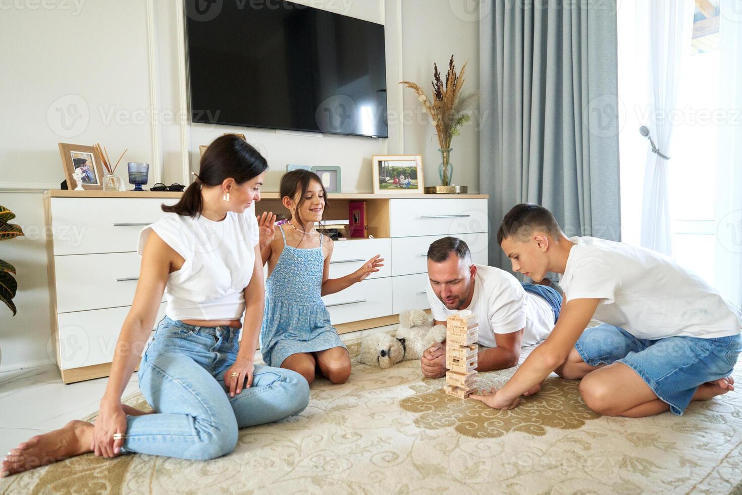 Family playing a jenga game on the floor in a bright living room during the afternoon photo