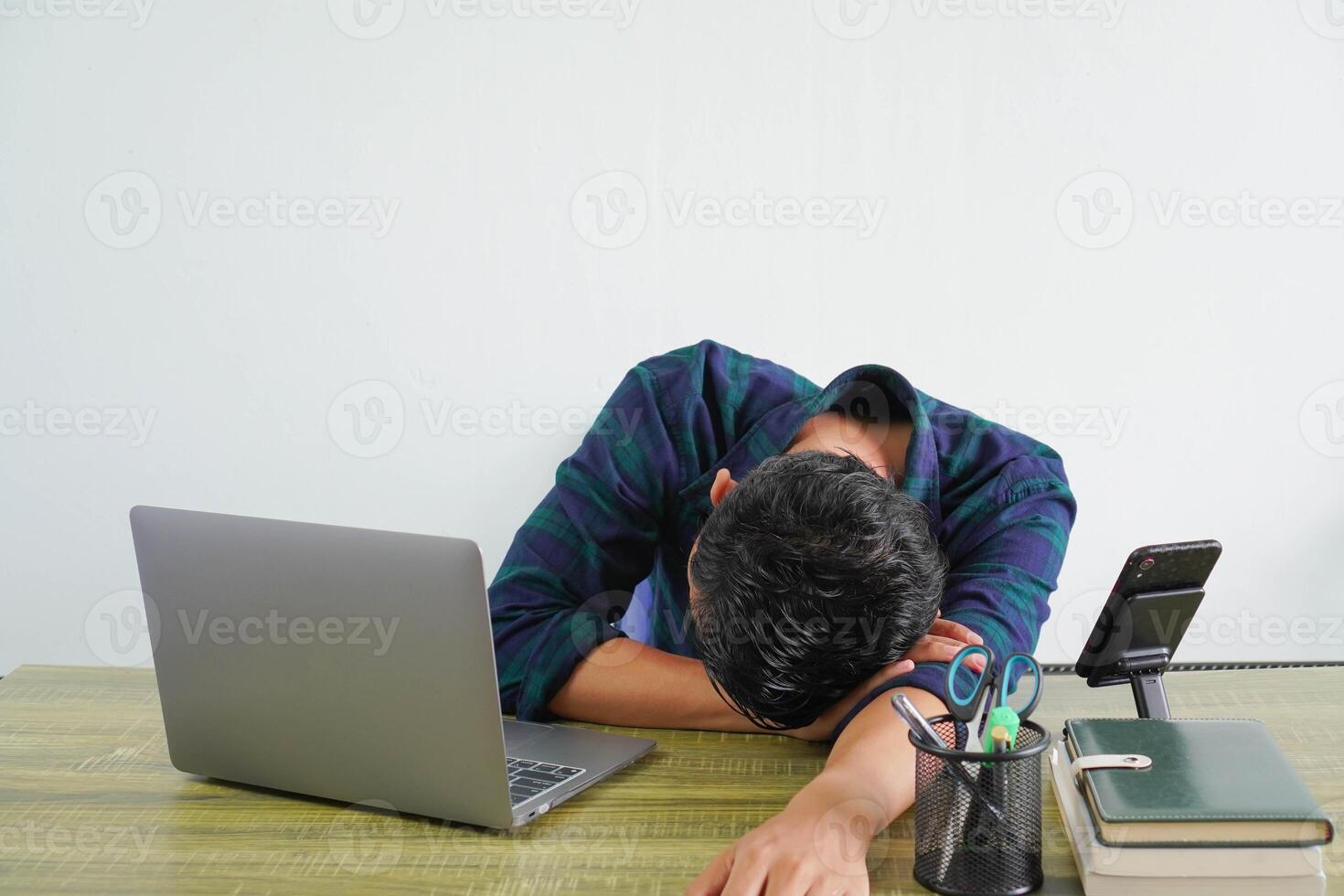 Tired young asian man in blue shirt sit work at wooden desk with pc laptop isolated on white background. Achievement business career lifestyle concept. Laid his head down on desk sleeping photo