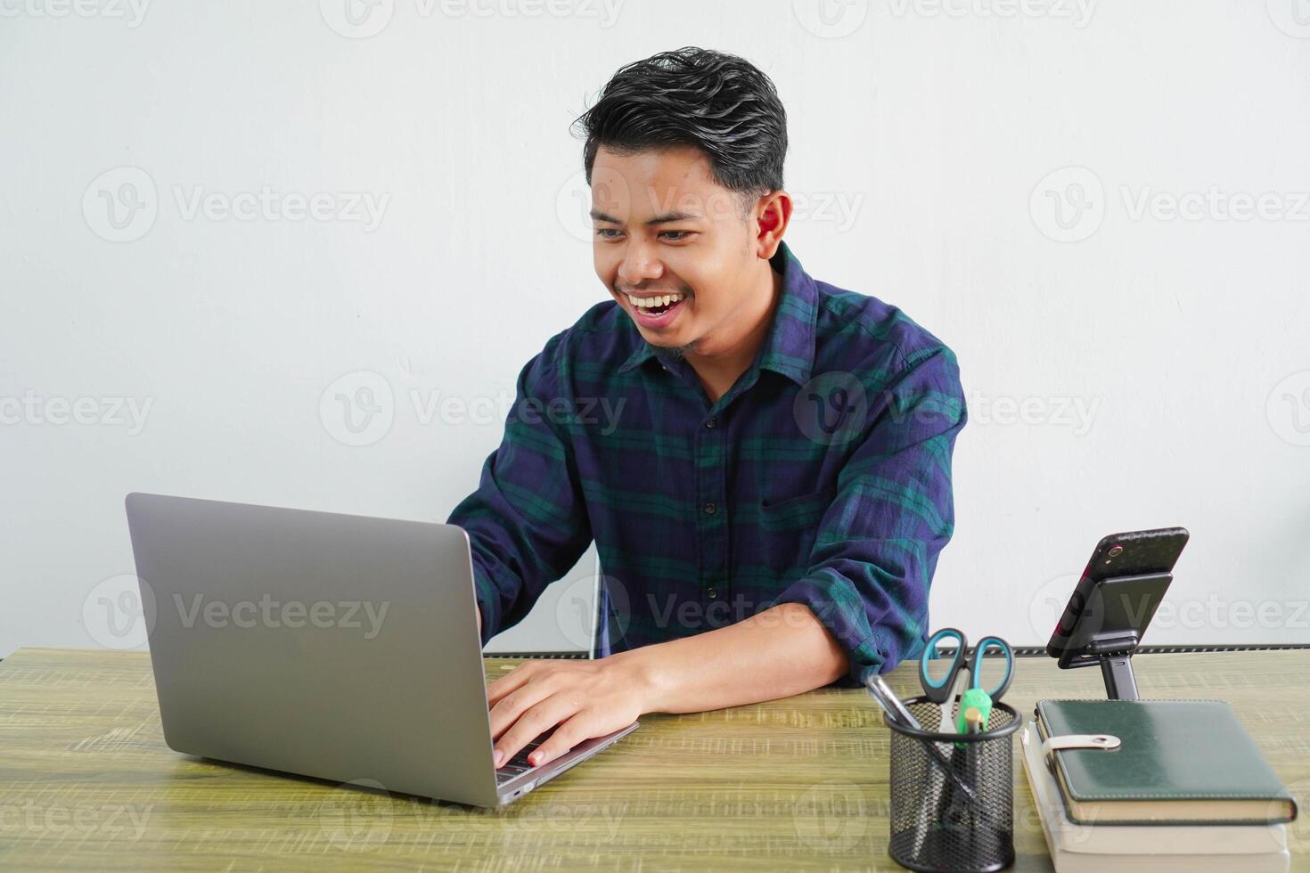 cheerful young asian man in blue shirt sit work at wooden desk with pc laptop isolated on white background. Achievement business career lifestyle concept. working on project with laptop pc computer photo