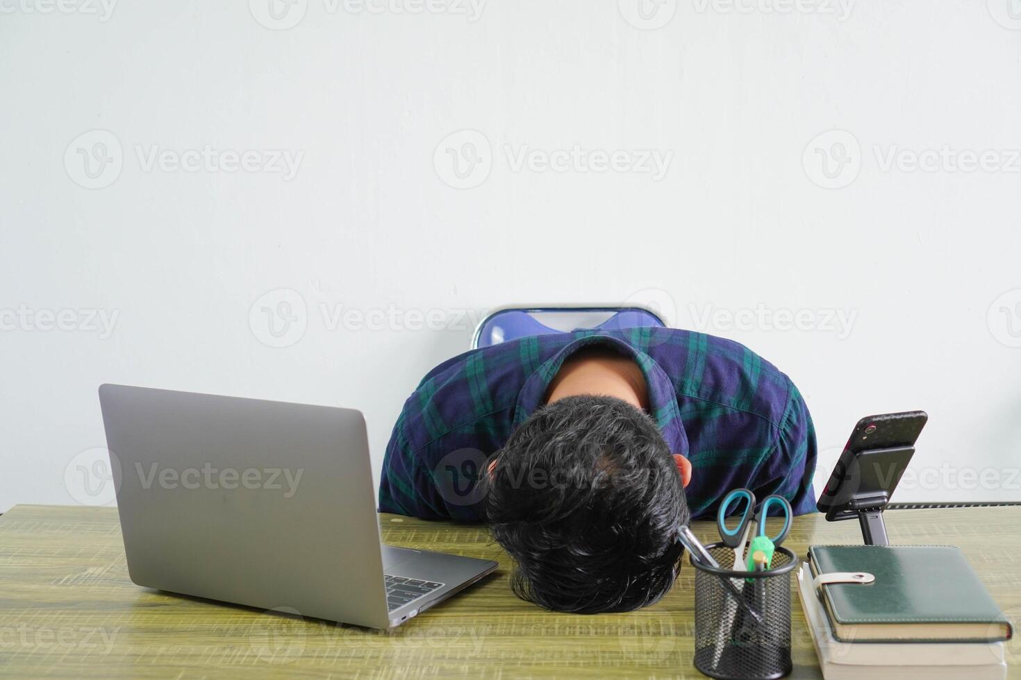 Exhausted young asian man in blue shirt sit work at wooden desk with pc laptop isolated on white background. Achievement business career lifestyle concept. laid his head down on desk photo