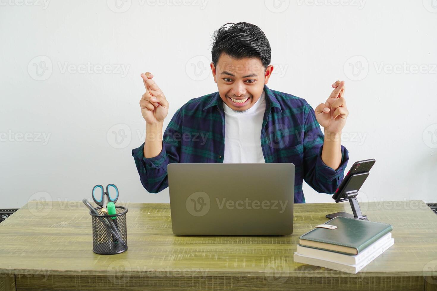 freelancer young asian man in his office with his fingers crossing shocked expression photo