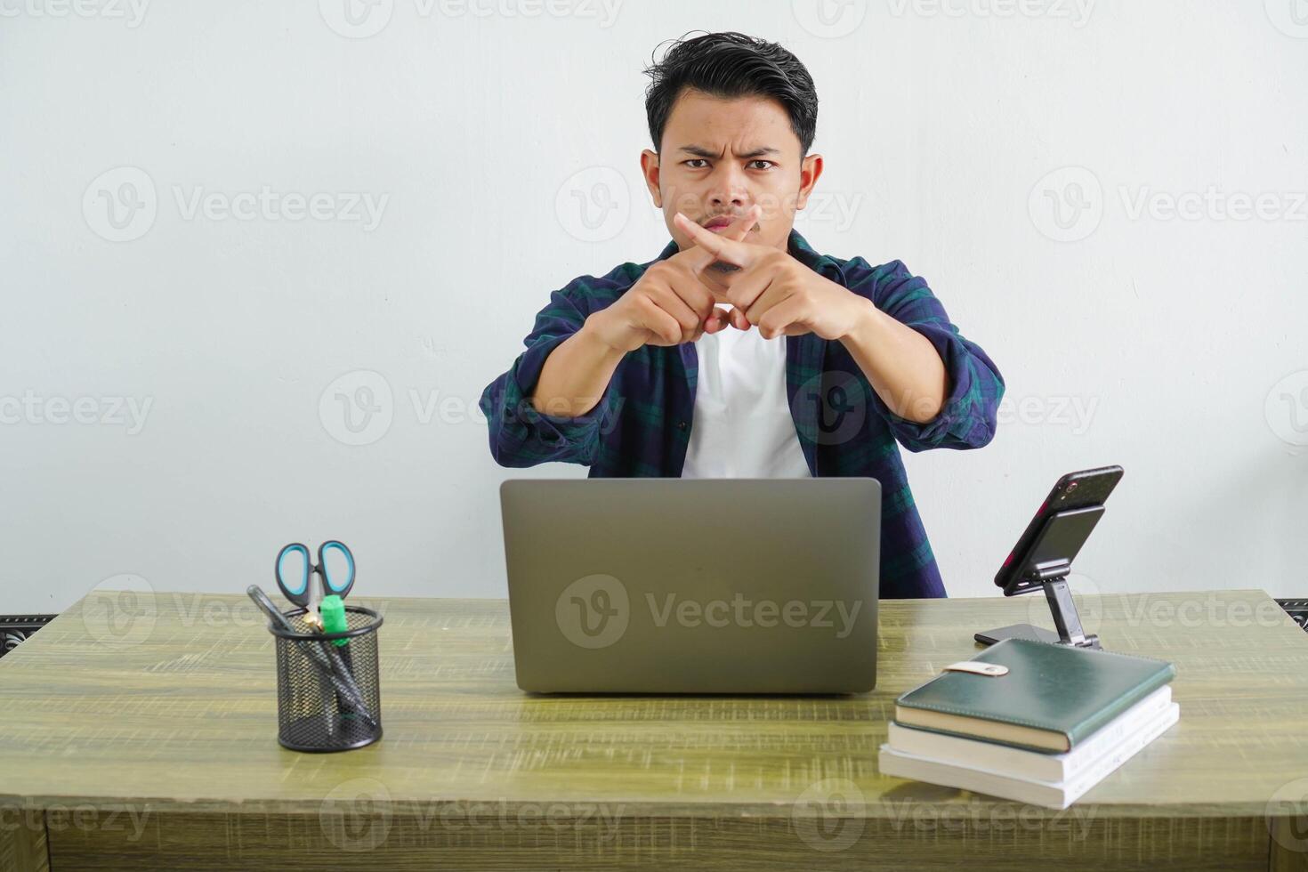 young asian businessman sitting at workplace doing gesture of rejection photo
