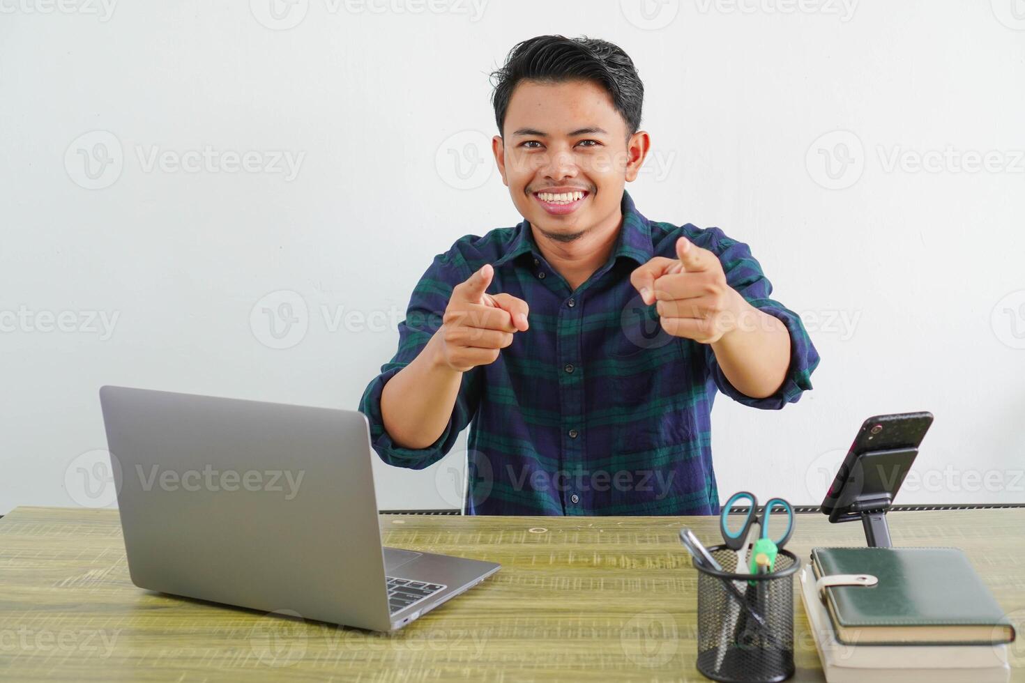 happy young asian man sit work at wooden desk with pc laptop. Achievement business career lifestyle concept. while pointing your finger forward photo