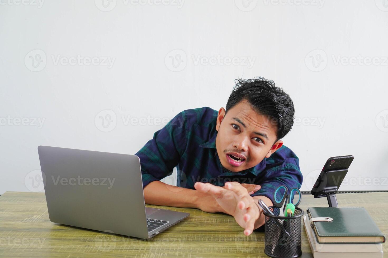 Tired perplexed young asian man sit work at wooden desk with pc laptop. Achievement business career lifestyle concept. laying on desk with outstretched hand photo