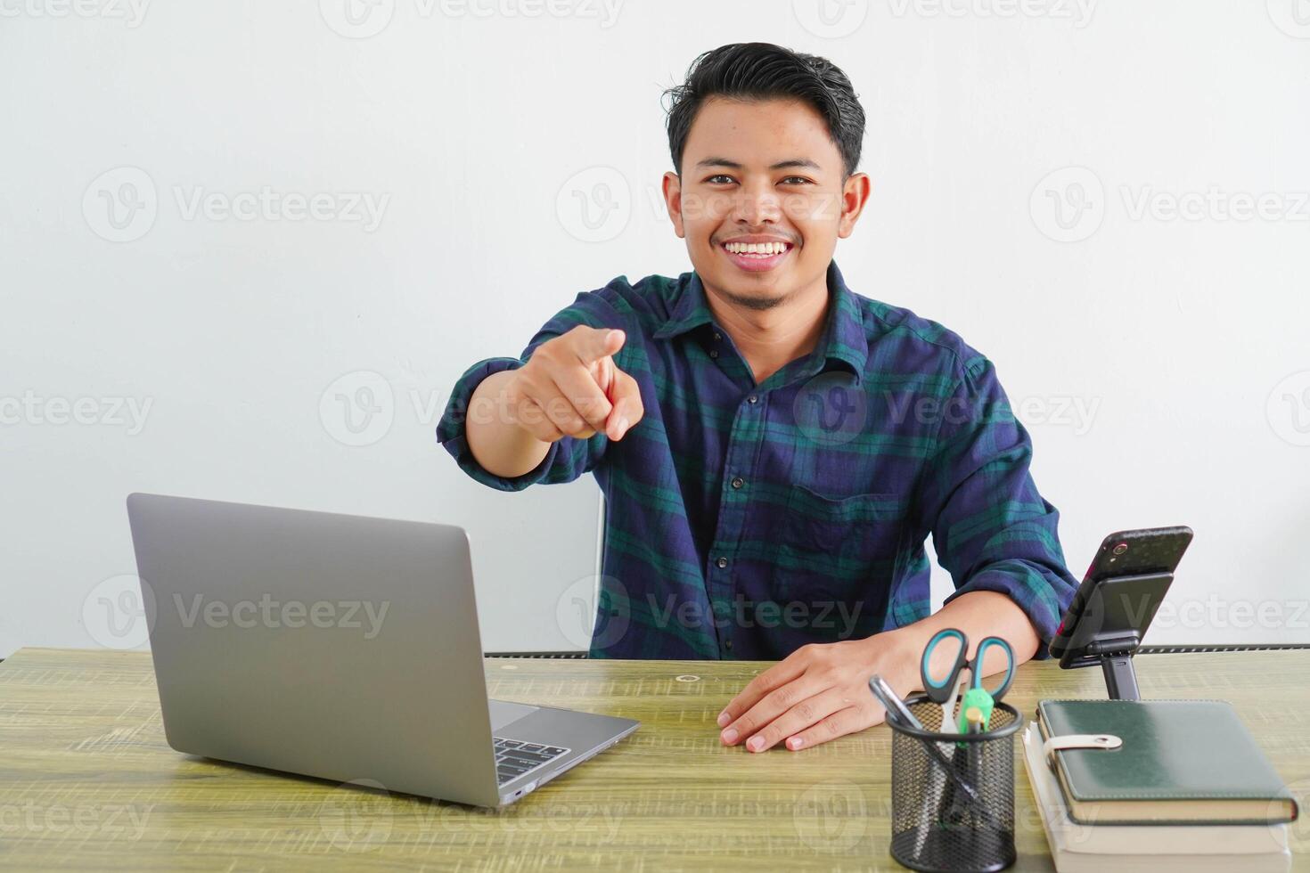 happy young asian man sit work at wooden desk with pc laptop. Achievement business career lifestyle concept. while pointing your finger forward photo
