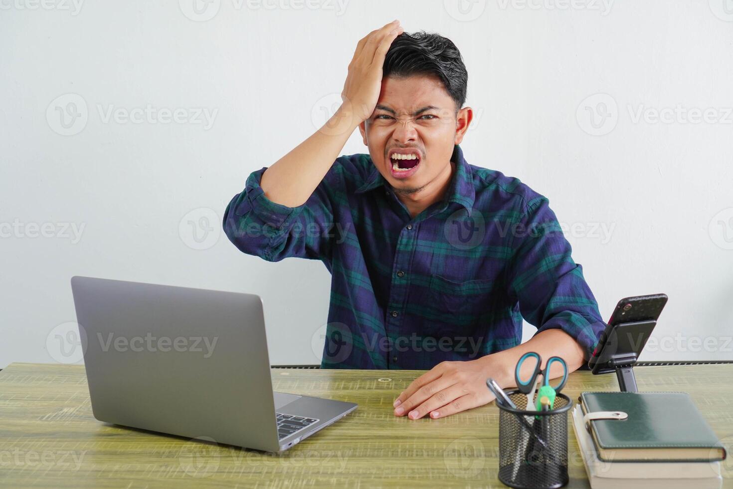 Irritated young asian man sit work at wooden desk with pc laptop. Achievement business career lifestyle concept. put hand on head photo