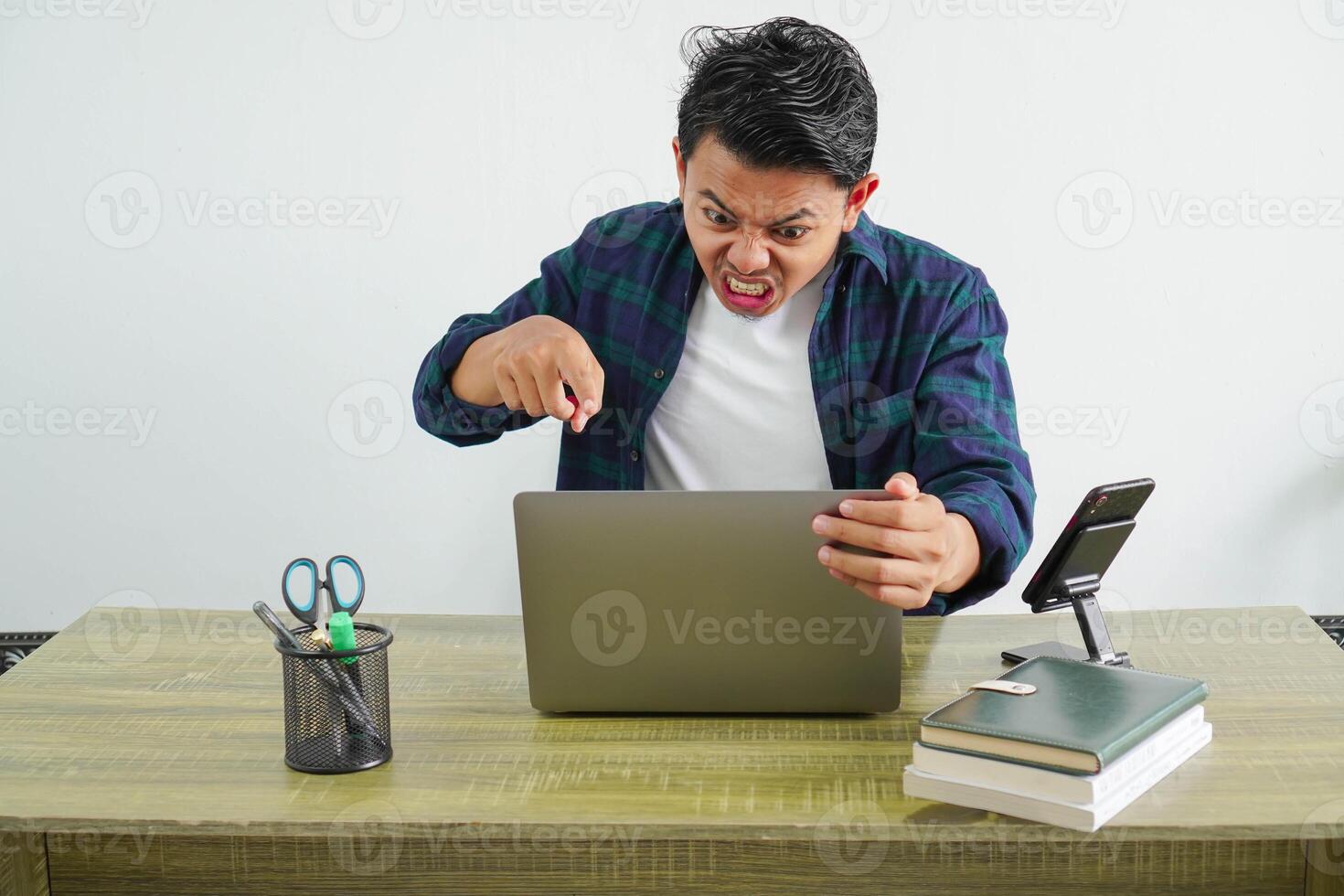 angry asian businessman is sitting at his workplace shouted and pointed at the laptop screen photo