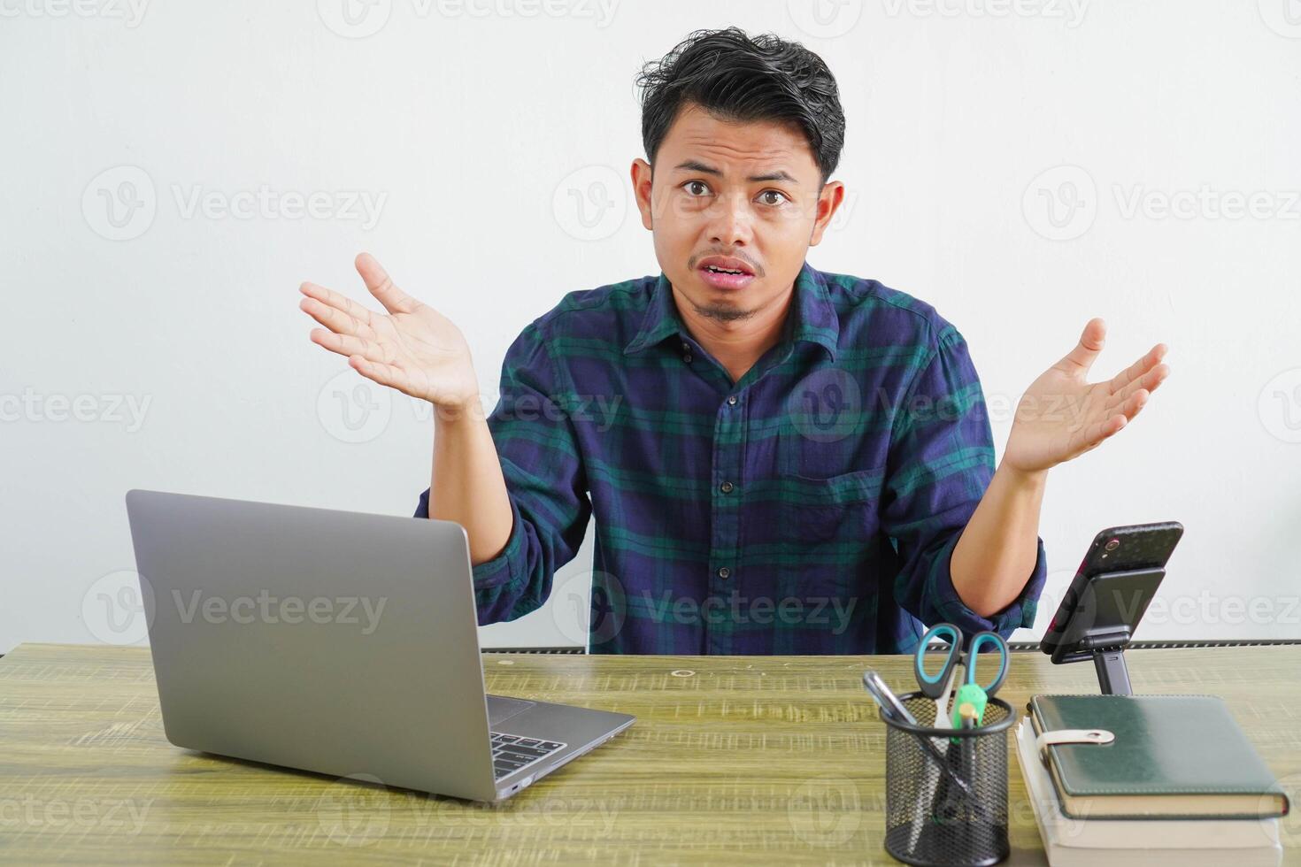 perplexed young asian man sit work at wooden desk with pc laptop. Achievement business career lifestyle concept. spreading hands photo