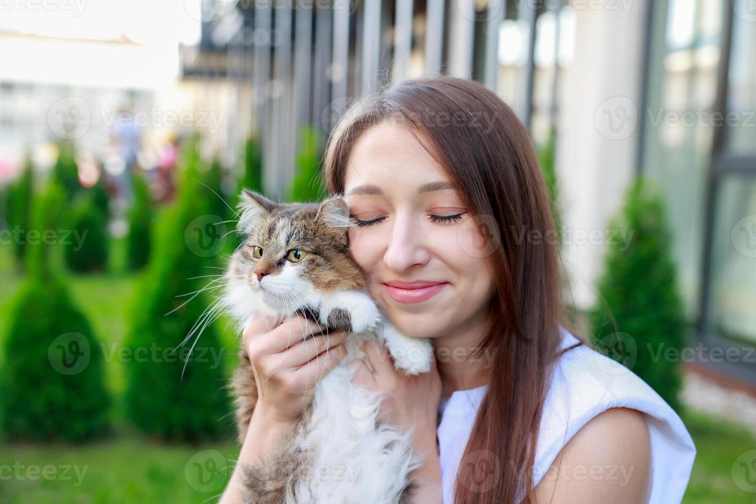 young woman lovingly cuddles her fluffy tabby cat outdoors, eyes closed in a moment of joy greenery photo