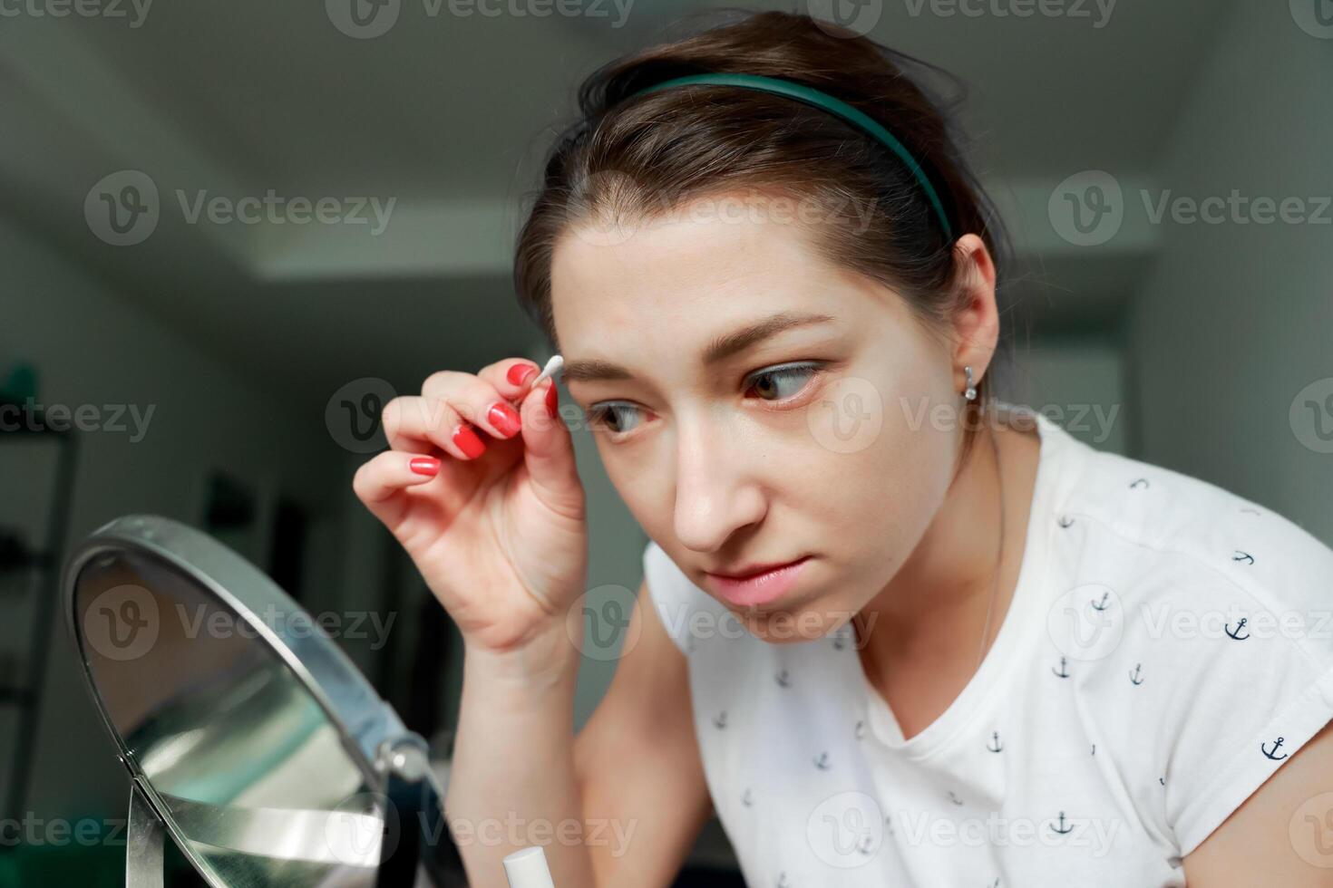 Young girl correcting her makeup in front of the mirror. Home makeup and self-care concept. photo