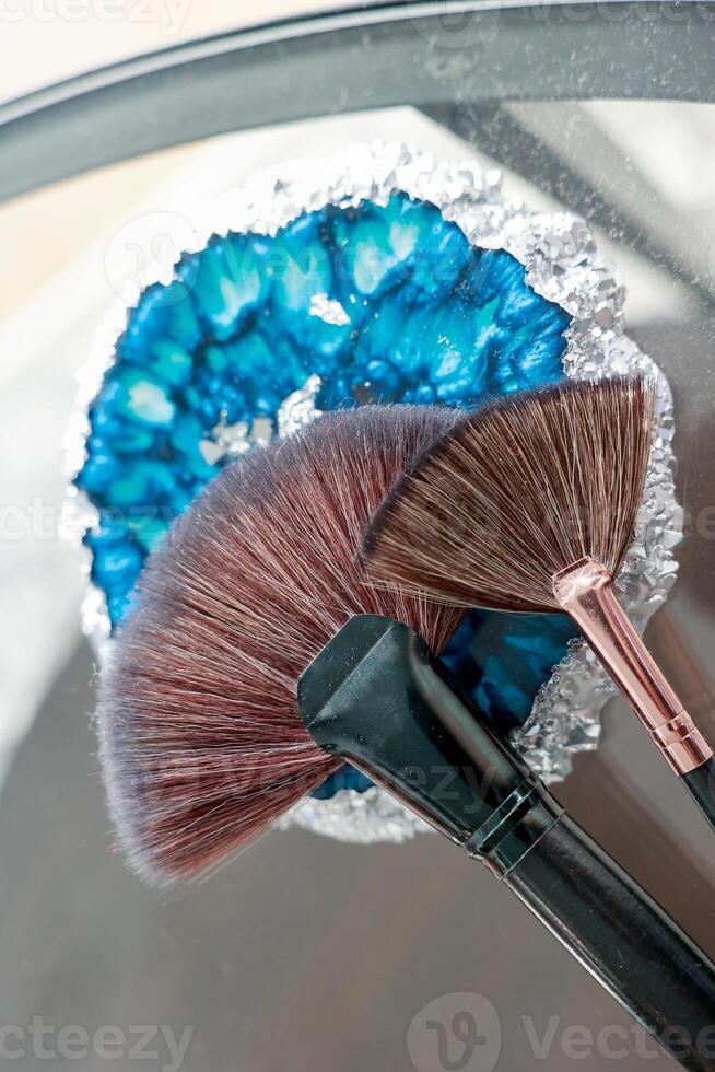 Two fan-shaped makeup brushes lying on a glass surface. photo