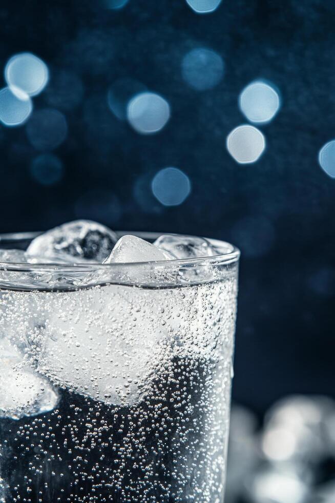 A refreshing glass of sparkling water with ice cubes on a dark background photo