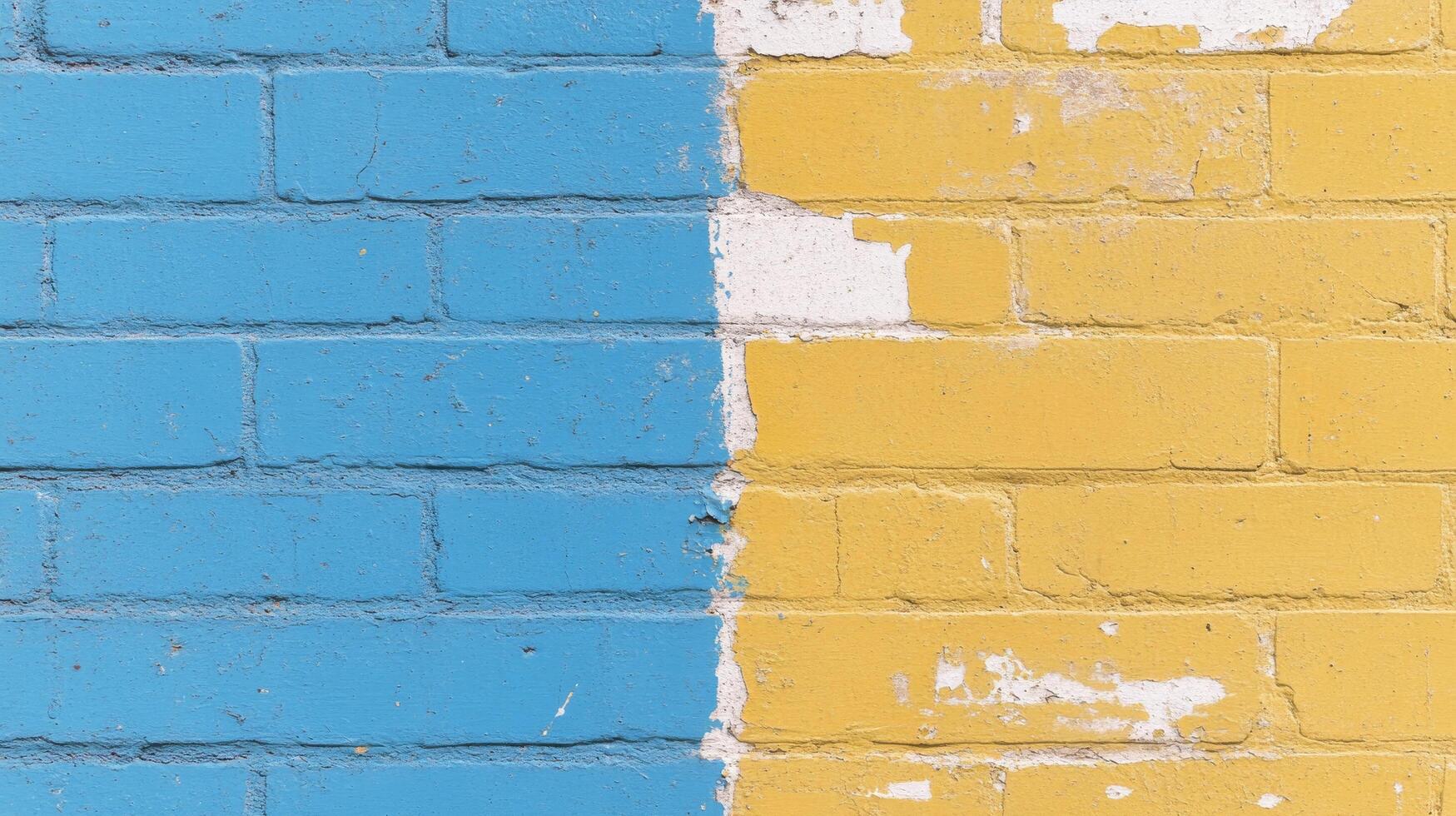 Two-tone brick wall divided into blue and yellow sections with peeling paint in urban setting photo