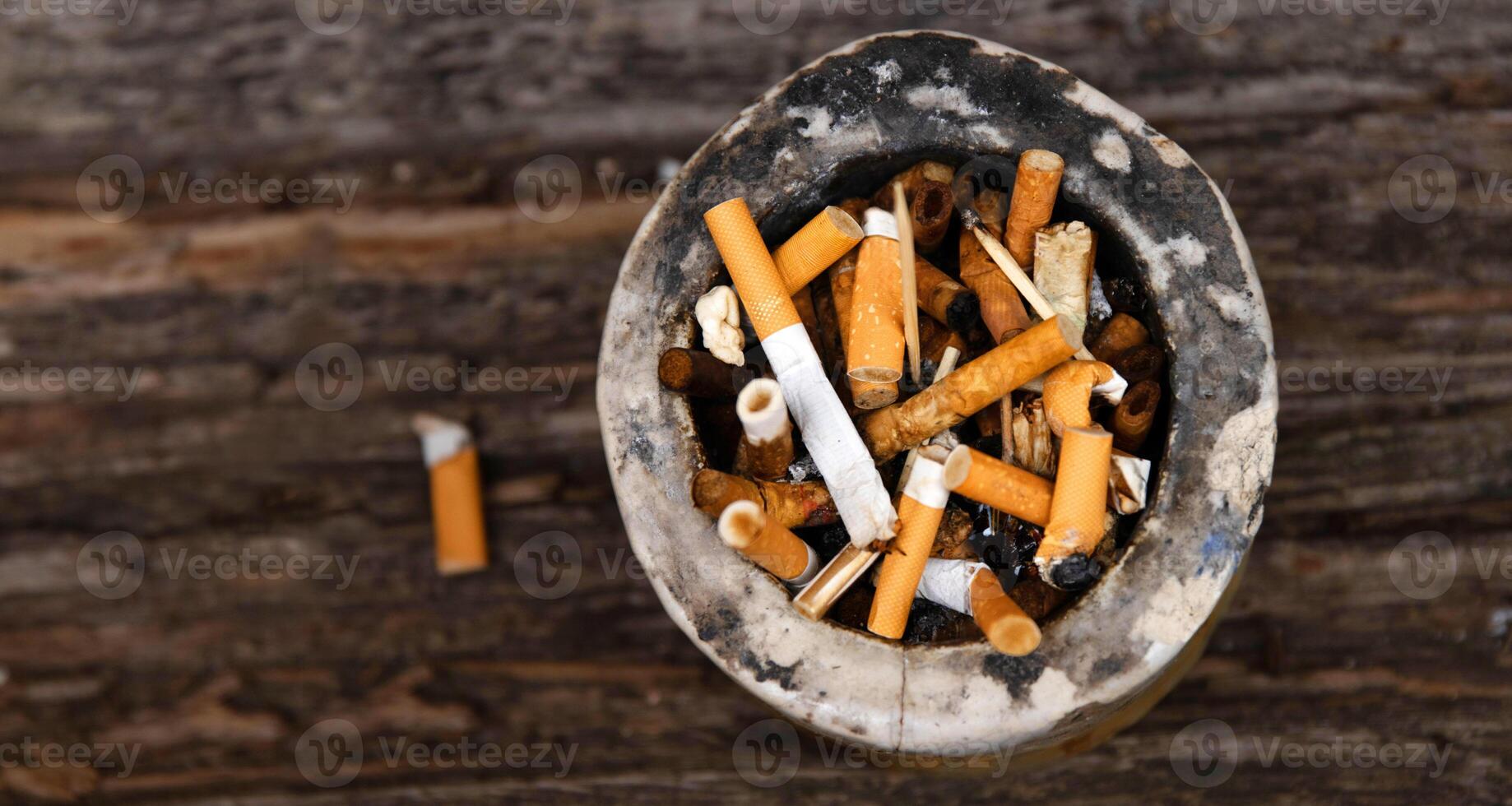 Closeup of an ashtray filled with numerous cigarette butts on a wooden surface, symbolizing smoking habits and litter, smoking harm, urban pollution, unhealthy lifestyle, littering. photo