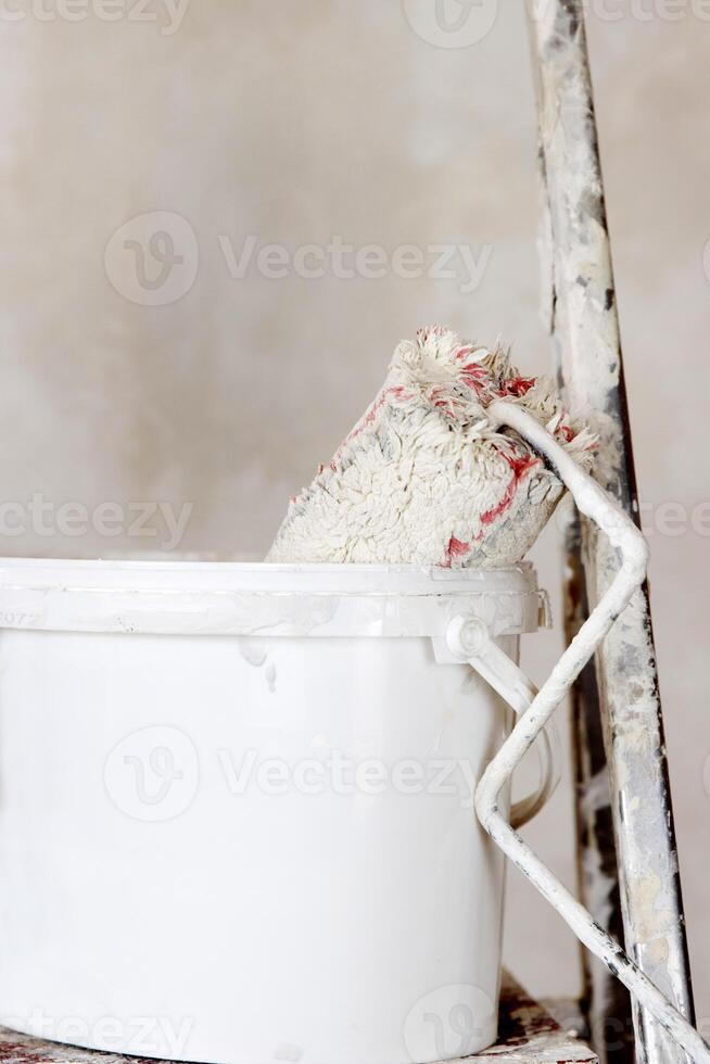 A white paint bucket with a used roller, positioned on a ladder. Perfect set for home painting and renovation. Essential tools for DIY home repair and construction work. Closeup. Copy space photo