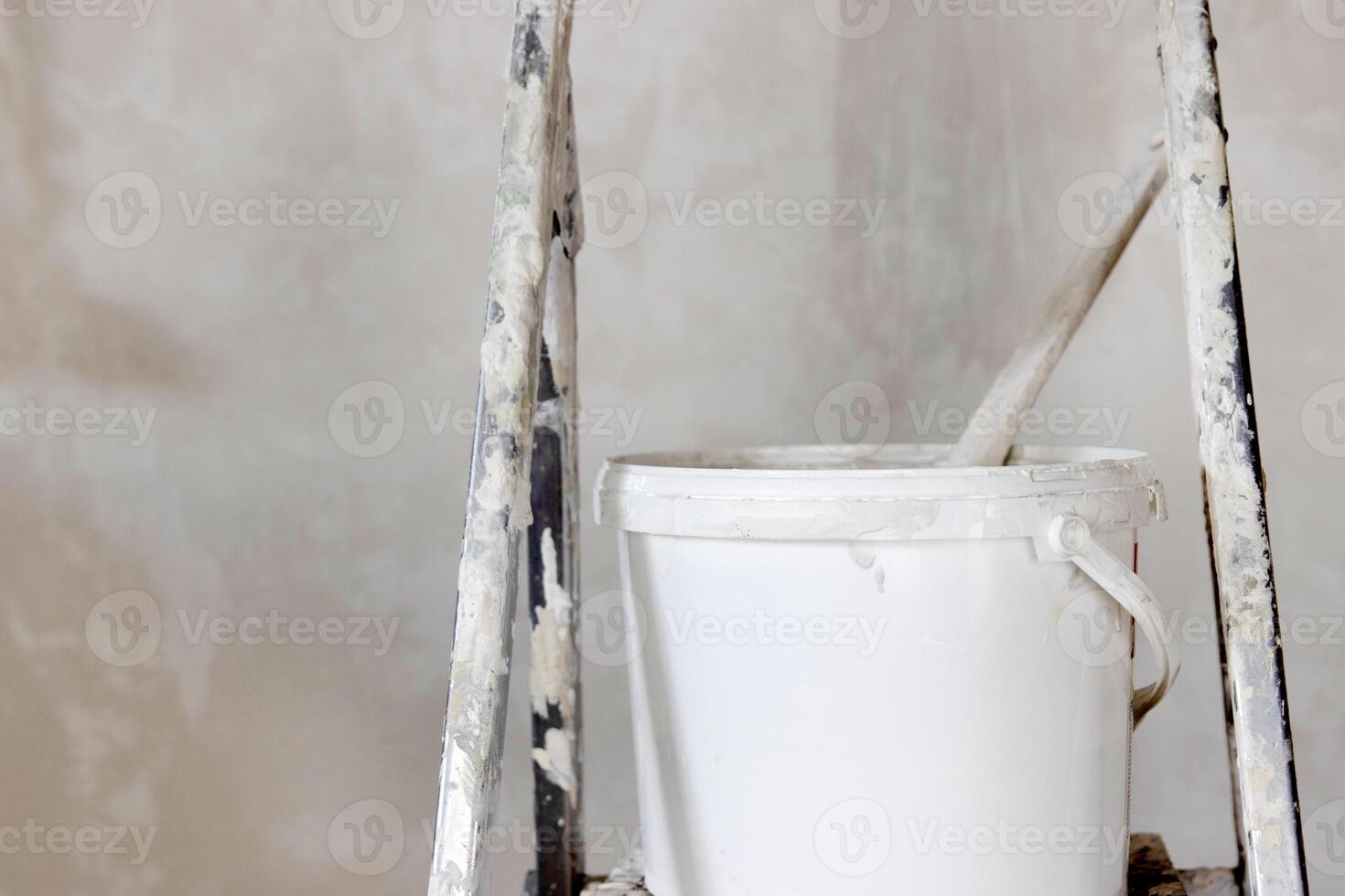A white paint bucket with a used roller, positioned on a ladder. Perfect set for home painting and renovation. Essential tools for DIY home repair and construction work. Closeup. Copy space photo