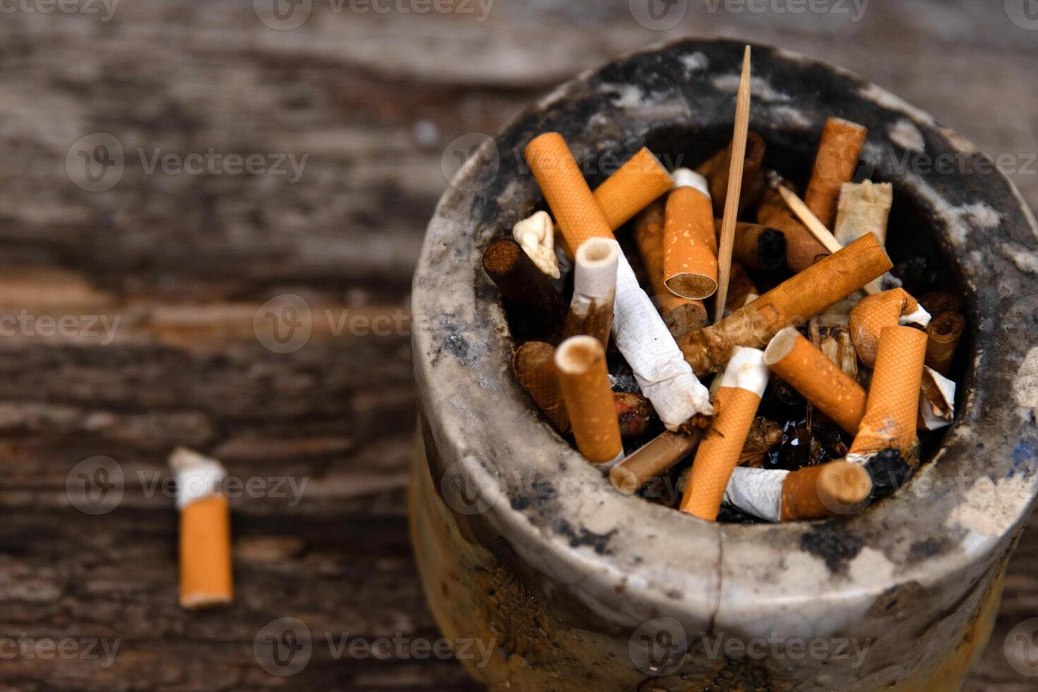 Closeup of an ashtray filled with numerous cigarette butts on a wooden surface, symbolizing smoking habits and litter, smoking harm, urban pollution, unhealthy lifestyle, littering. photo
