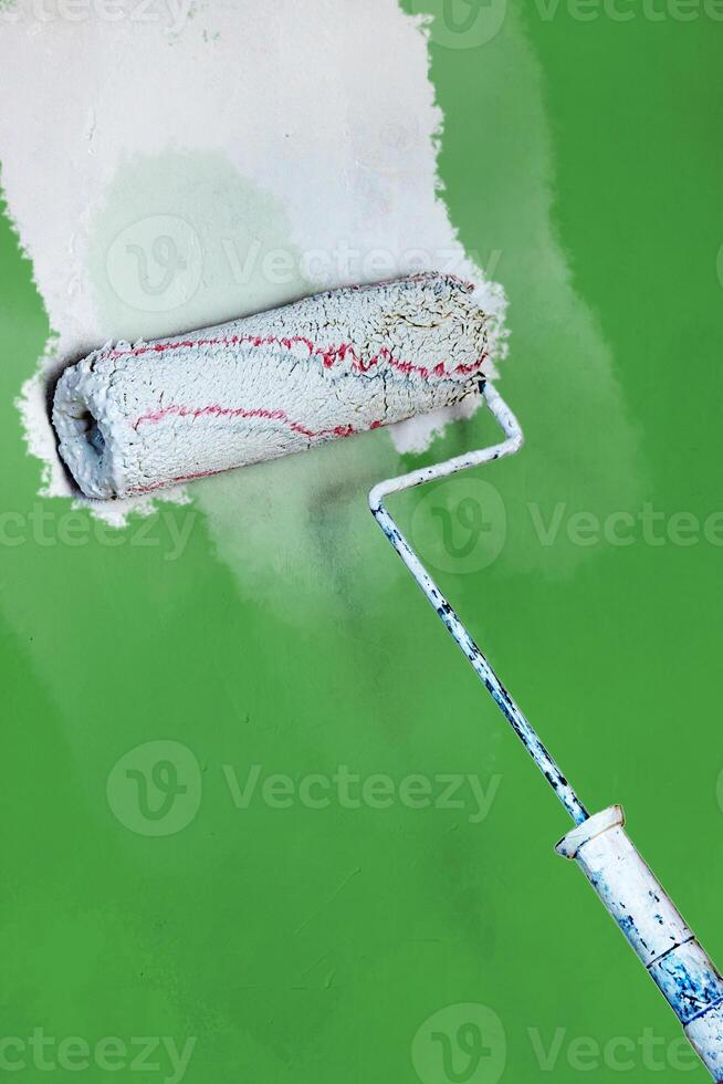 Creative graphic concept of paint roller applying fresh white color paint onto the green concrete wall. Process of home renovation, improvement and makeover. Copy space. photo